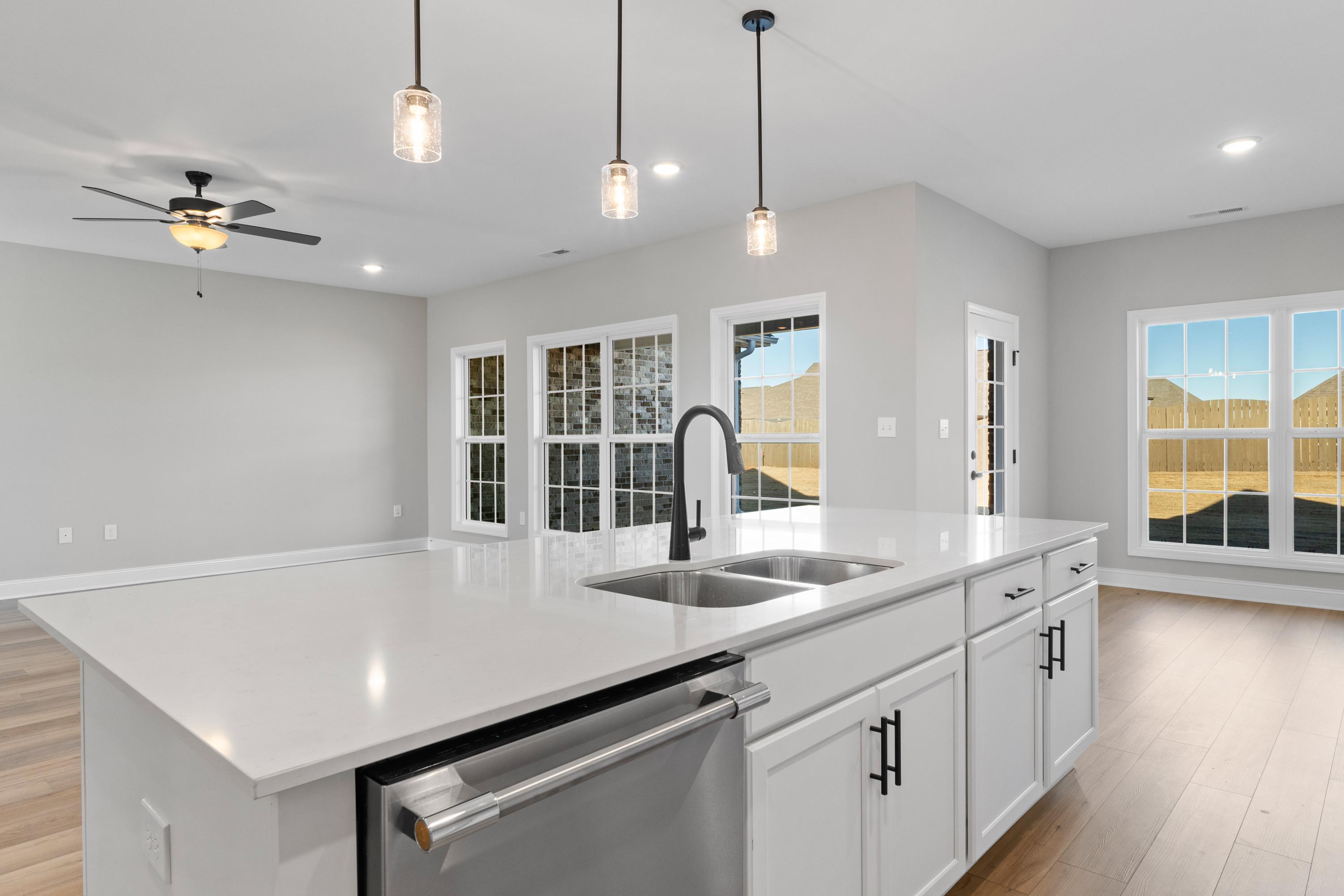 Spacious Valencia kitchen by Davidson Homes with white quartz island, black faucet sink, shaker cabinets, pendant lights, and large windows