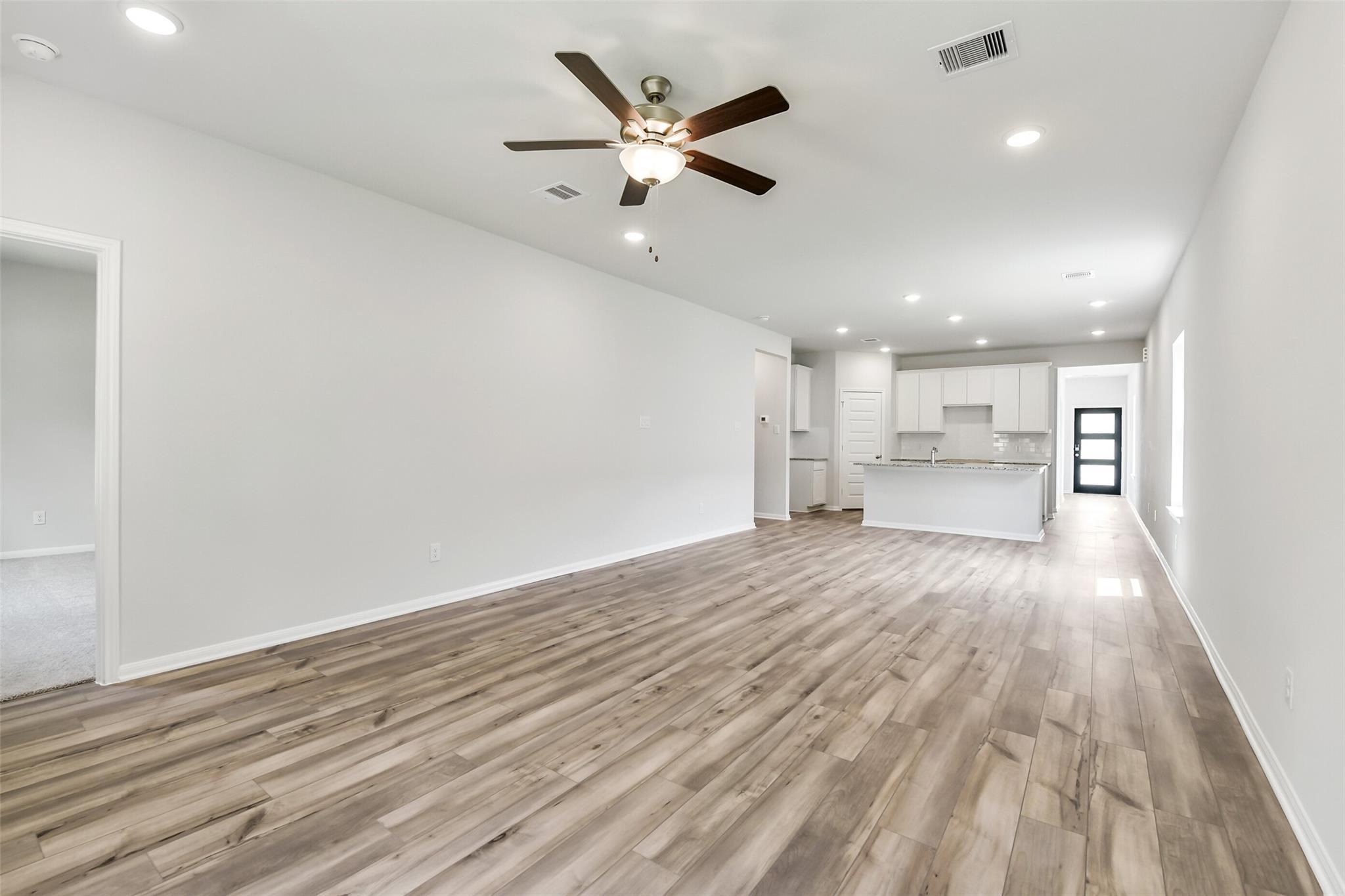 Open living room with hardwood floors, white walls, ceiling fan, and adjacent kitchen in The Sabine E 4-bedroom home, Conroe, Texas