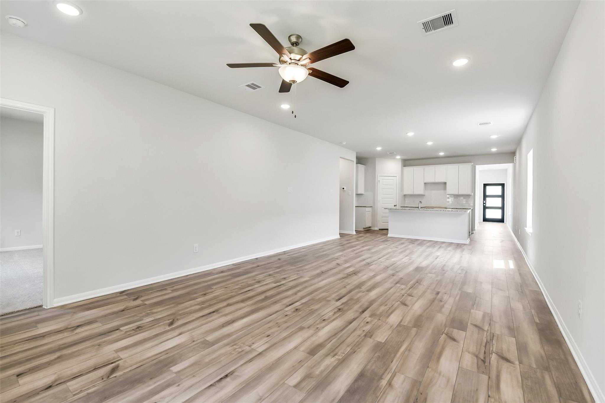 Open living room with hardwood floors, white walls, ceiling fan, and adjacent kitchen in The Sabine E 4-bedroom home, Conroe, Texas