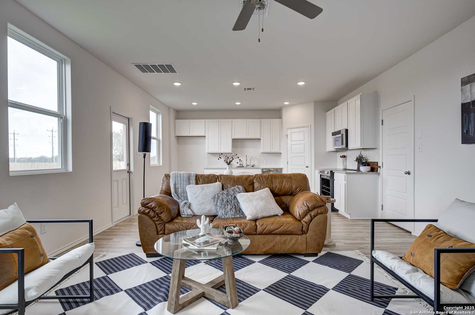Open-concept living room with brown leather sofa, glass coffee table, and white kitchen cabinets in Davidson Homes Trinity A, San Antonio