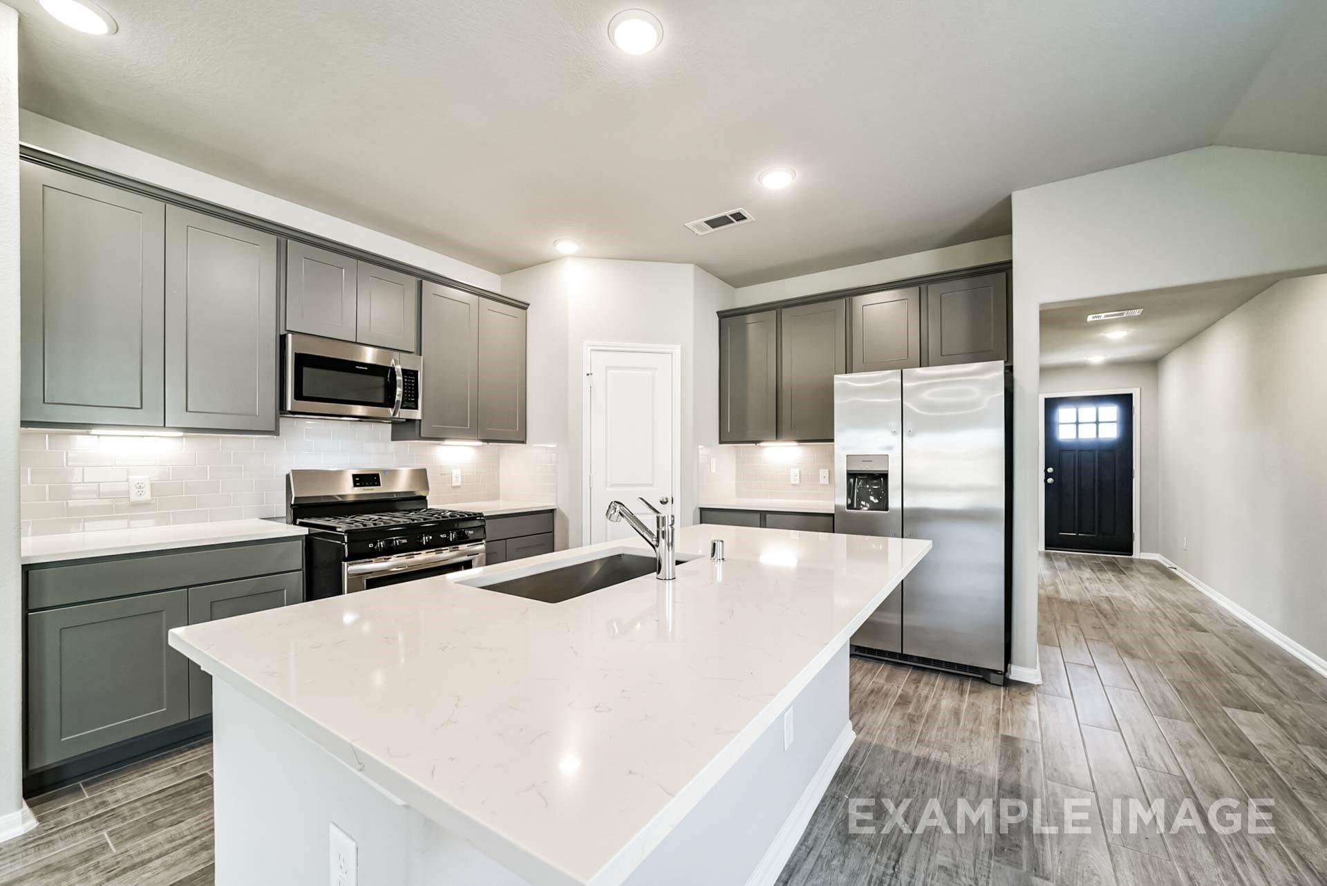 Modern kitchen with quartz island, grey cabinets, and stainless appliances in The Riviera A plan at Emberly, Beasley, TX.