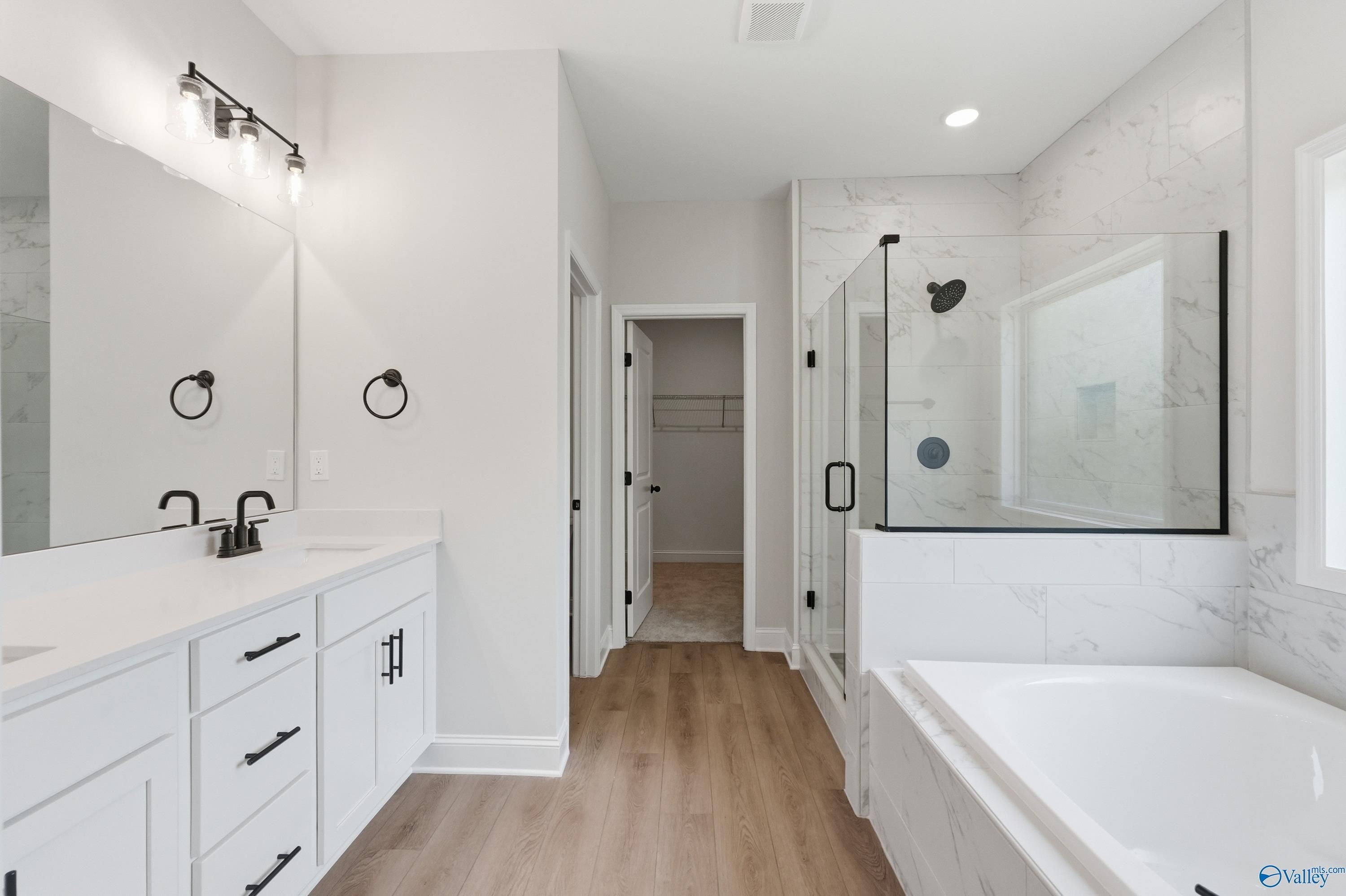 Elegant master bathroom with white double vanity, frameless glass shower, marble tiles, soaking tub in Davidson Homes The Rockford B, Athens AL