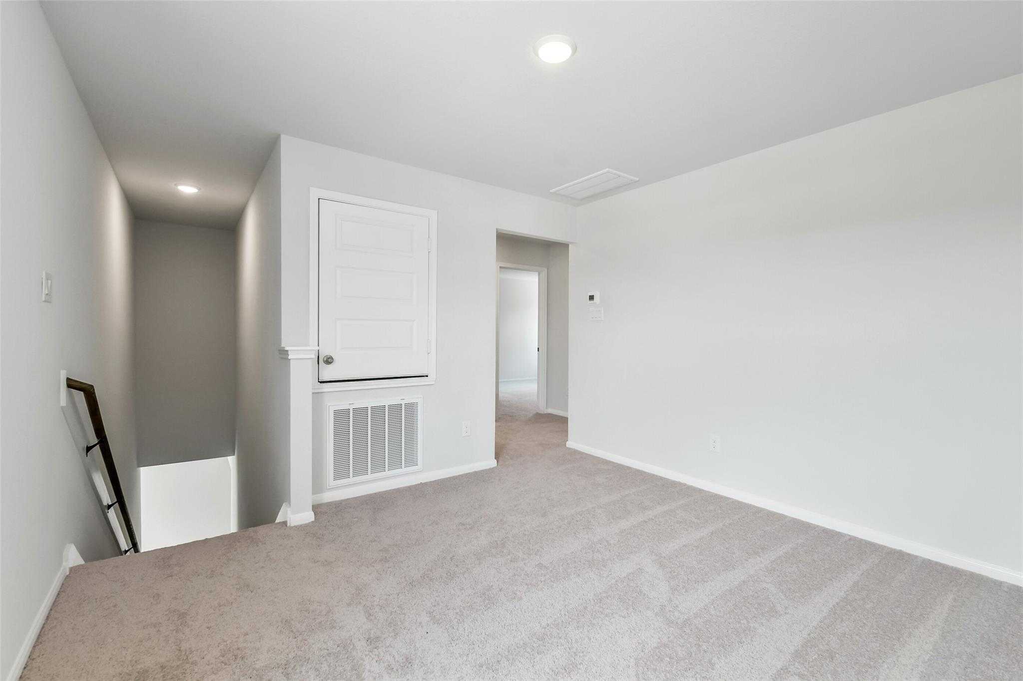 Spacious second-floor landing with beige carpet, white walls, open door, and staircase in Davidson Homes Sabine E, Conroe, Texas