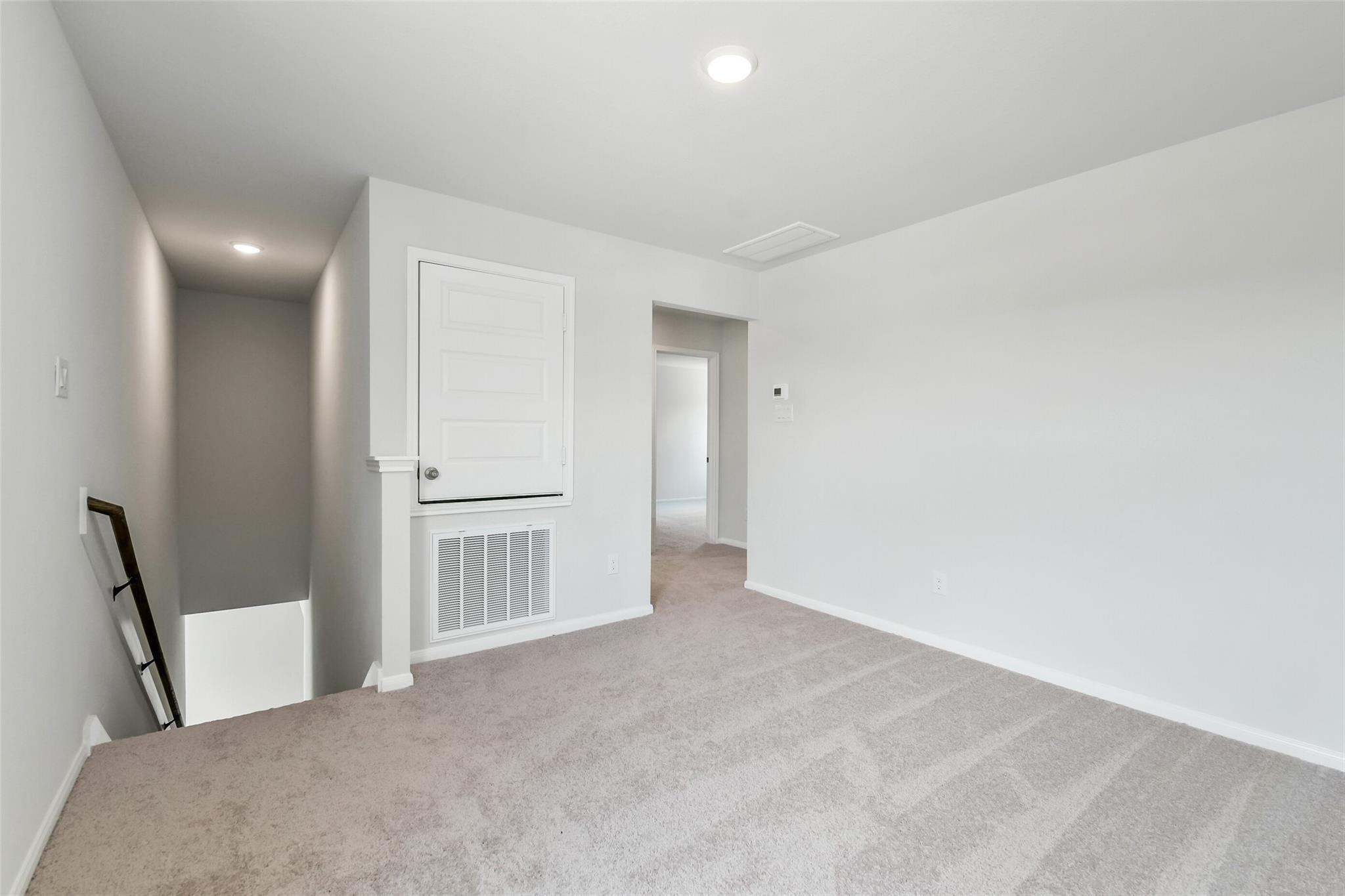 Spacious second-floor landing with beige carpet, white walls, open door, and staircase in Davidson Homes Sabine E, Conroe, Texas