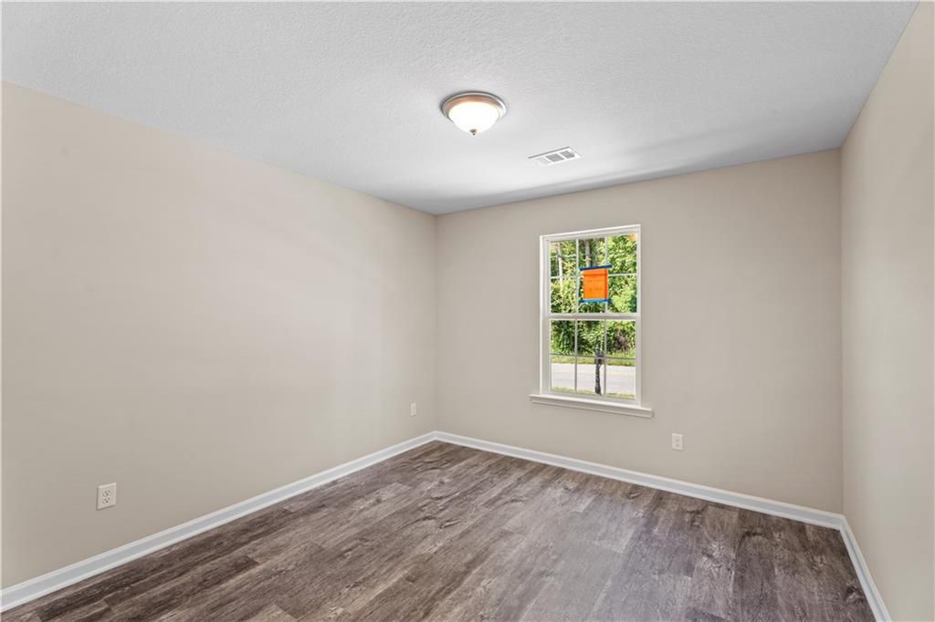 Bright bedroom with beige walls, hardwood floors, and window view of trees in Davidson Homes The Washington, Phenix City, Alabama