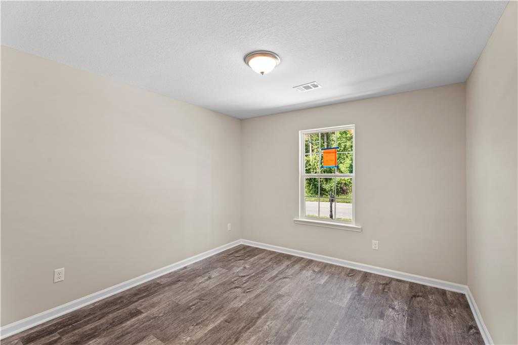 Bright bedroom with beige walls, hardwood floors, and window view of trees in Davidson Homes The Washington, Phenix City, Alabama