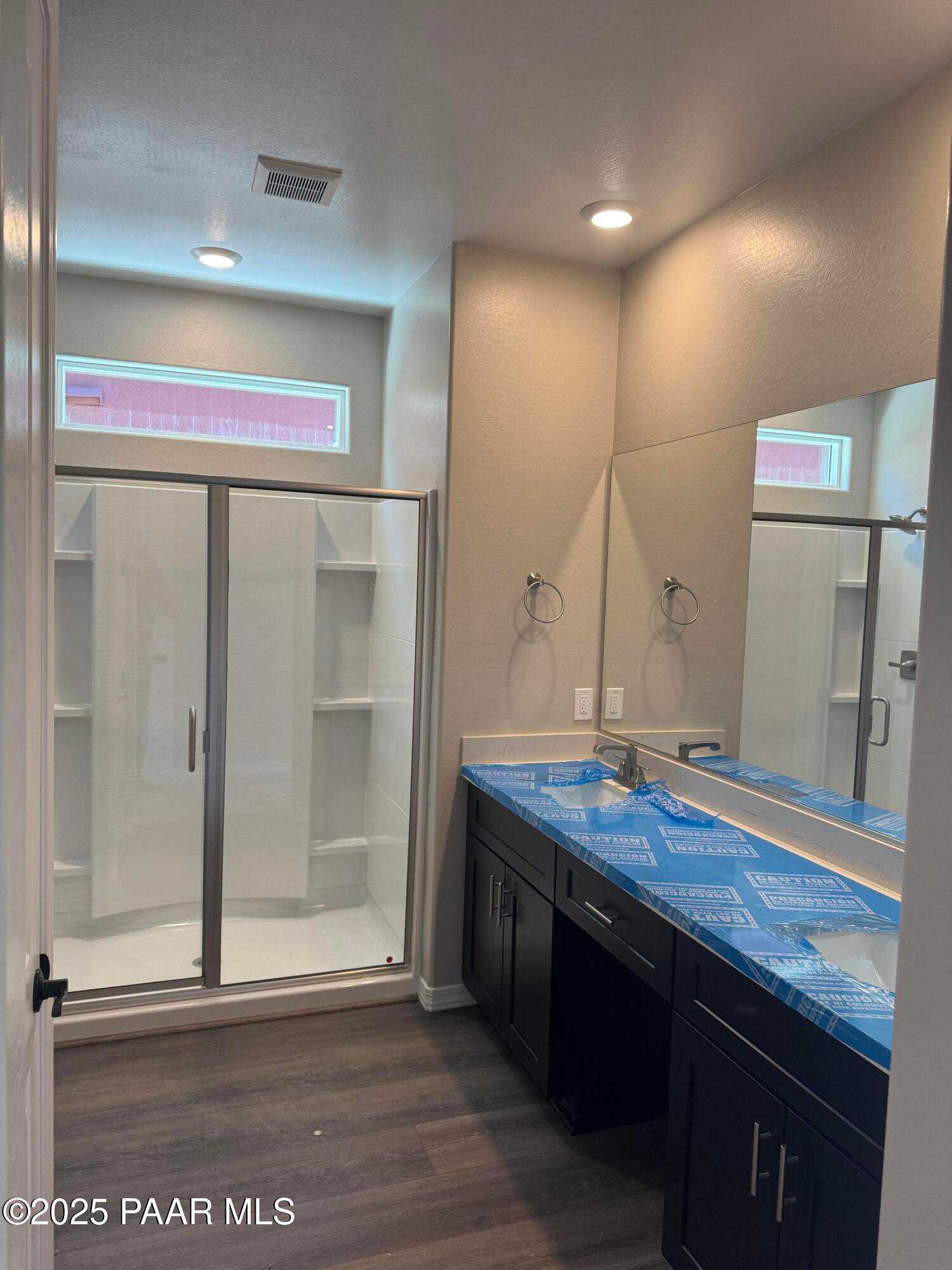 Modern master bathroom with frameless glass shower, double vanity, dark cabinets, and wood floors in Davidson Homes The Durango II A, Prescott, AZ