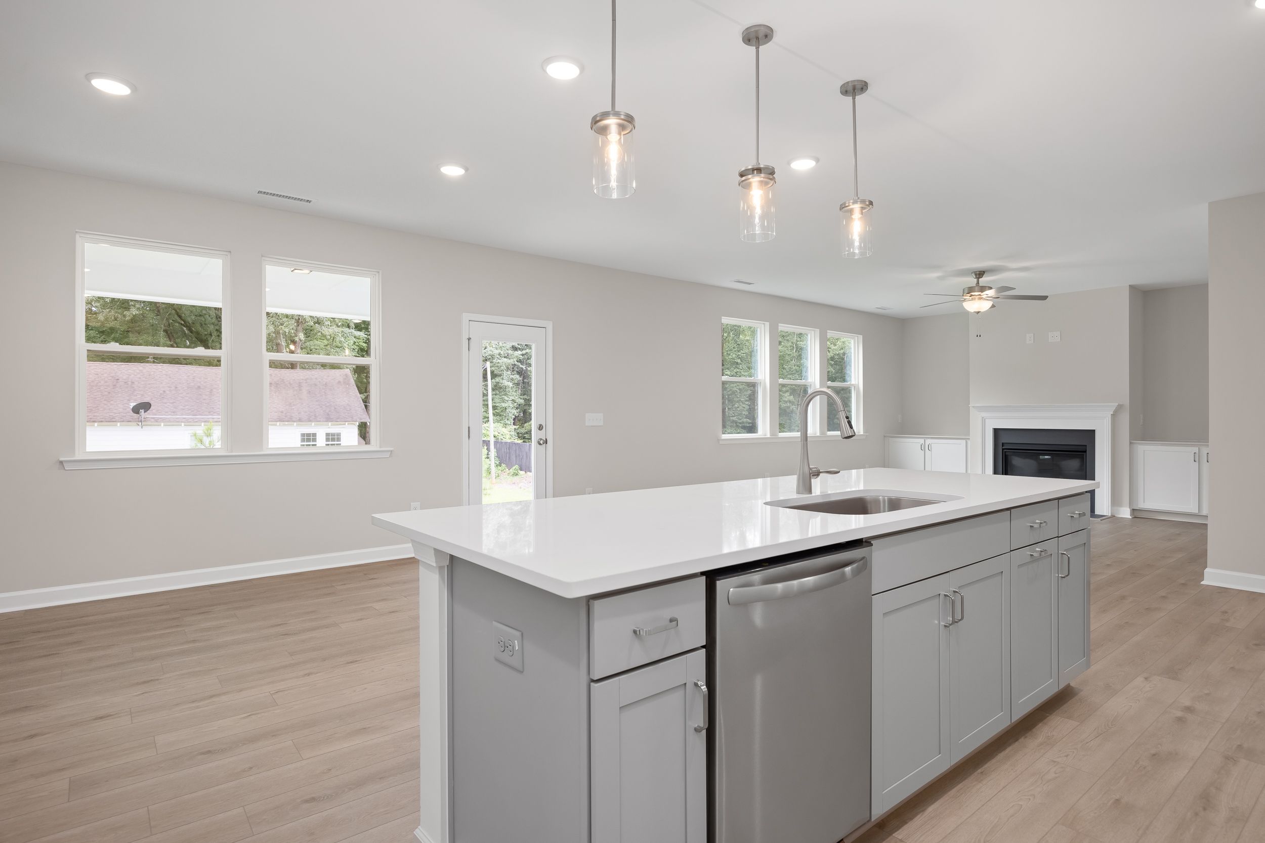 Spacious open-concept kitchen in The Beech A with white quartz island, stainless sink, gray shaker cabinets, pendant lights, and fireplace