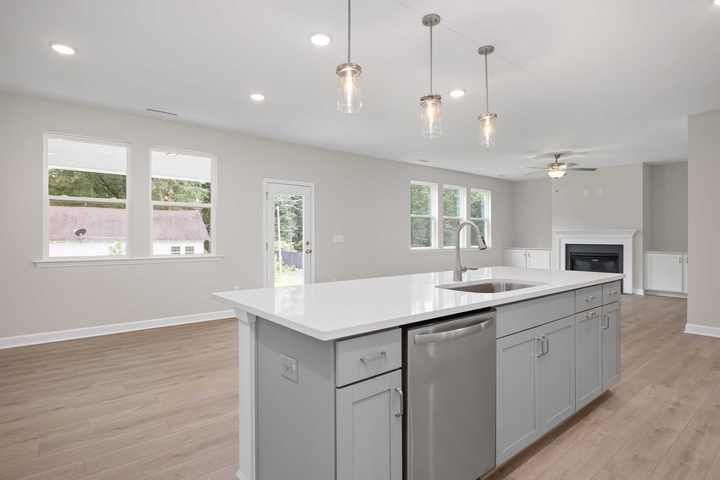Spacious open-concept kitchen in The Beech C by Davidson Homes, featuring white quartz island, stainless appliances, pendant lights, and fireplace living area