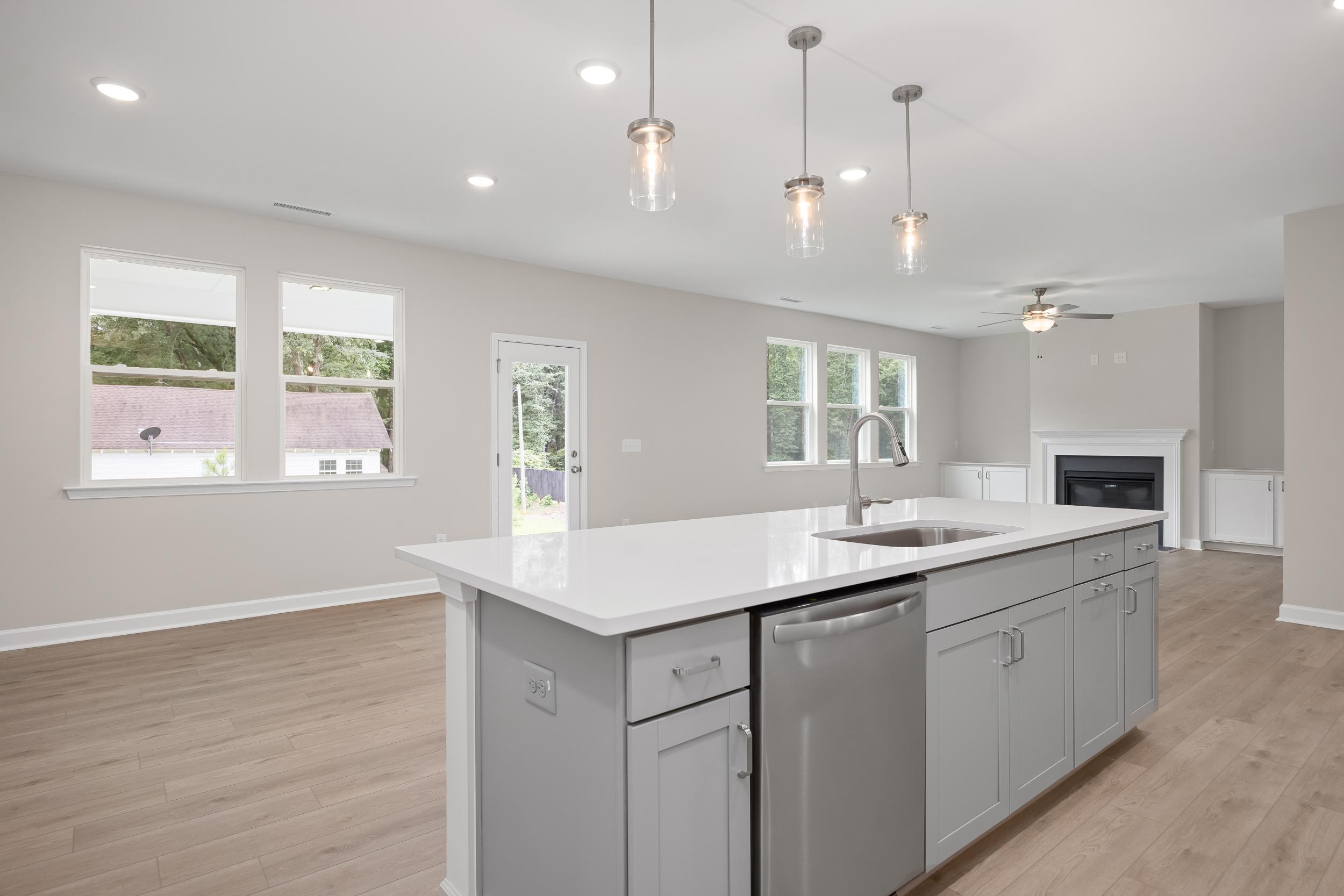 Spacious open-concept kitchen in The Beech A with white quartz island, stainless sink, gray shaker cabinets, pendant lights, and fireplace