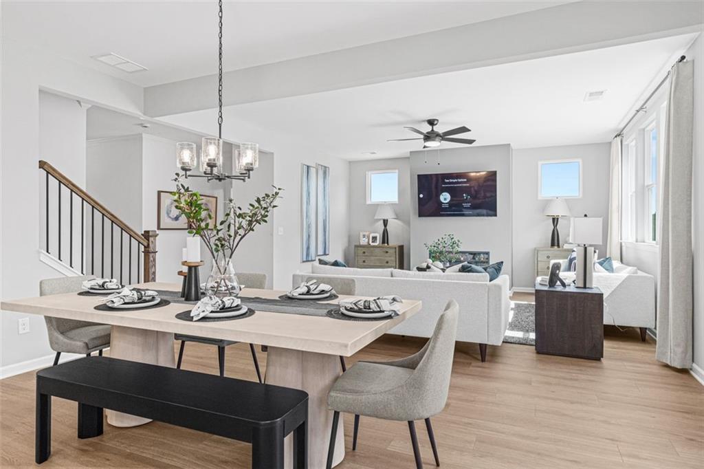 Open dining-living area with wooden table, chandelier, white sofa, wall TV in Davidson Homes The Hickory B 5-bedroom, Hoschton, GA