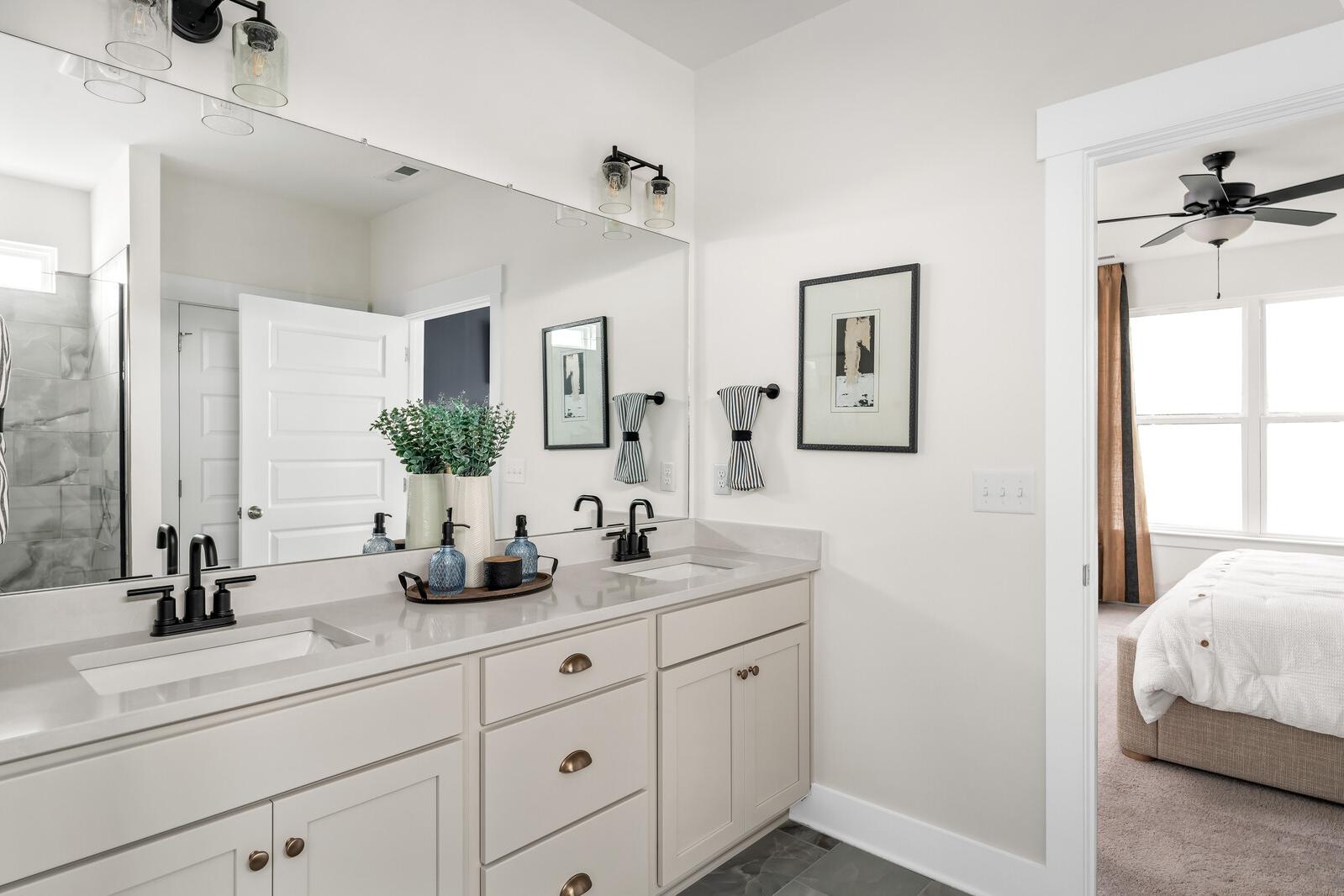 Spacious primary bathroom at Woods Crossing in Gallatin TN with double vanity, mirrors, greenery, and bedroom view
