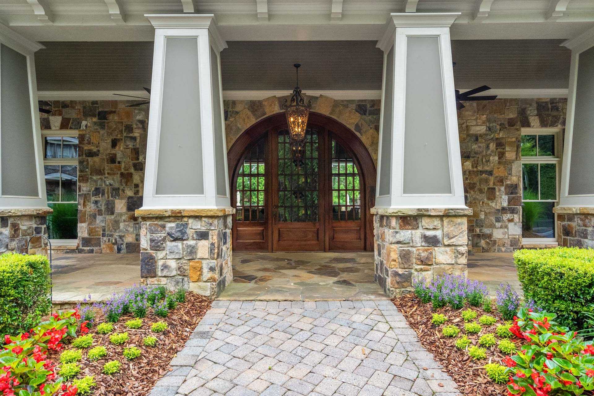 Rustic Craftsman home entrance at The Village at Towne Lake Woodstock GA with arched wooden door stone columns and paver path