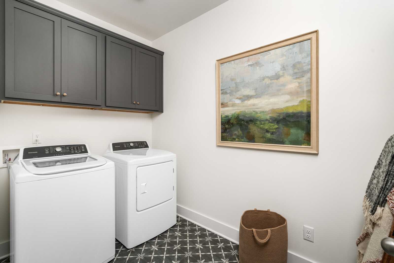 Spacious laundry room at Woods Crossing in Gallatin TN with white washer dryer, gray cabinets, abstract art, and patterned tile floor