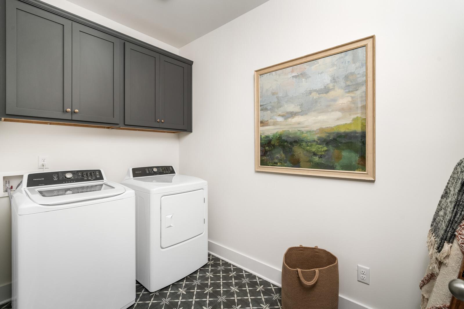 Spacious laundry room at Woods Crossing in Gallatin TN with white washer dryer, gray cabinets, abstract art, and patterned tile floor