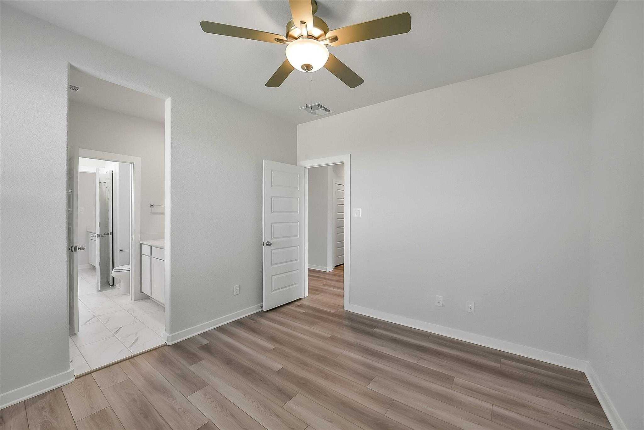 Bright secondary bedroom with en-suite bath, ceiling fan, and laminate floors in Davidson Homes The Acadia A, Katy, Texas