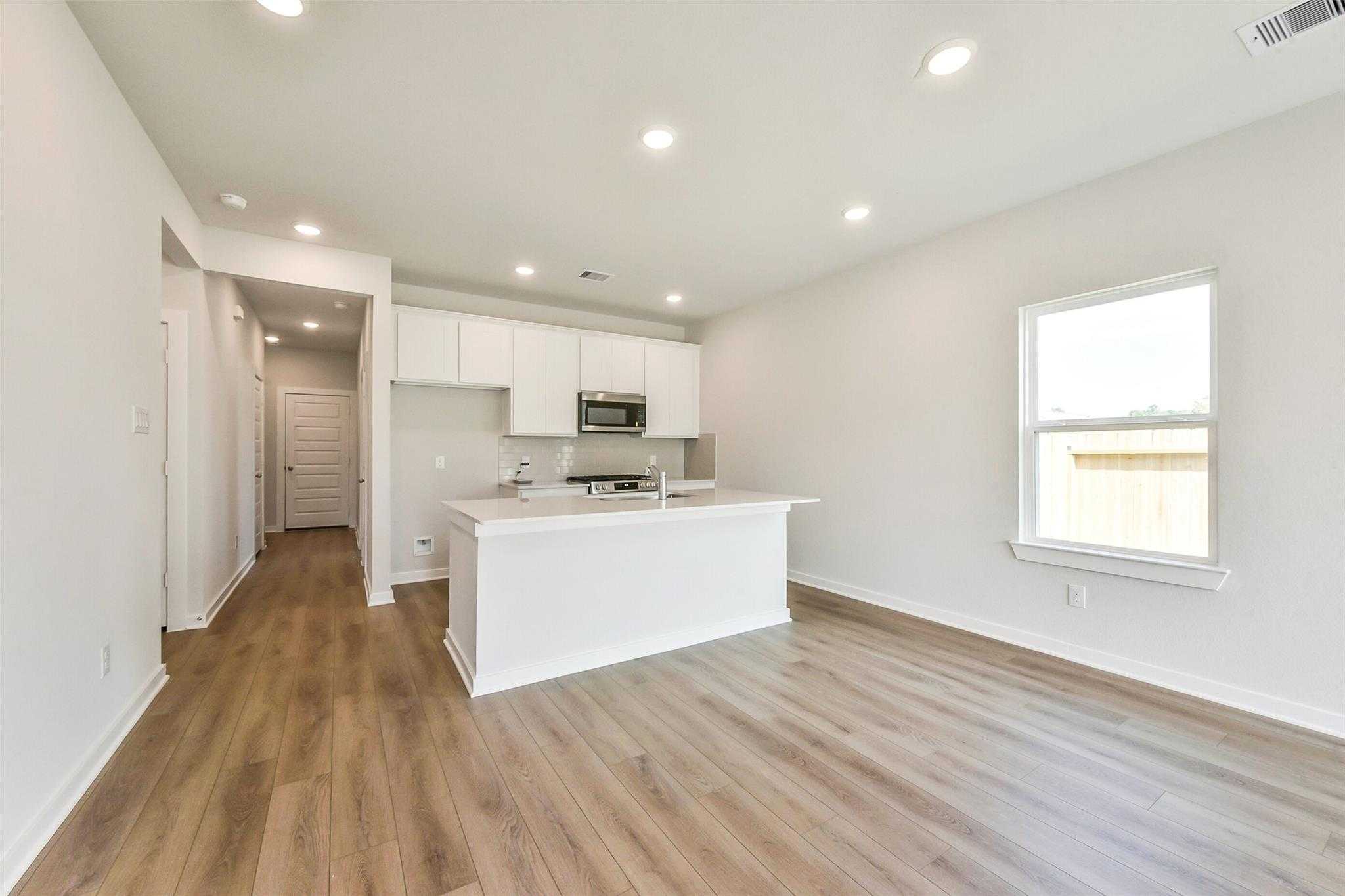 Open-concept white kitchen with island sink, stainless microwave, and backyard view in Davidson Homes The Comal G, Dayton, Texas