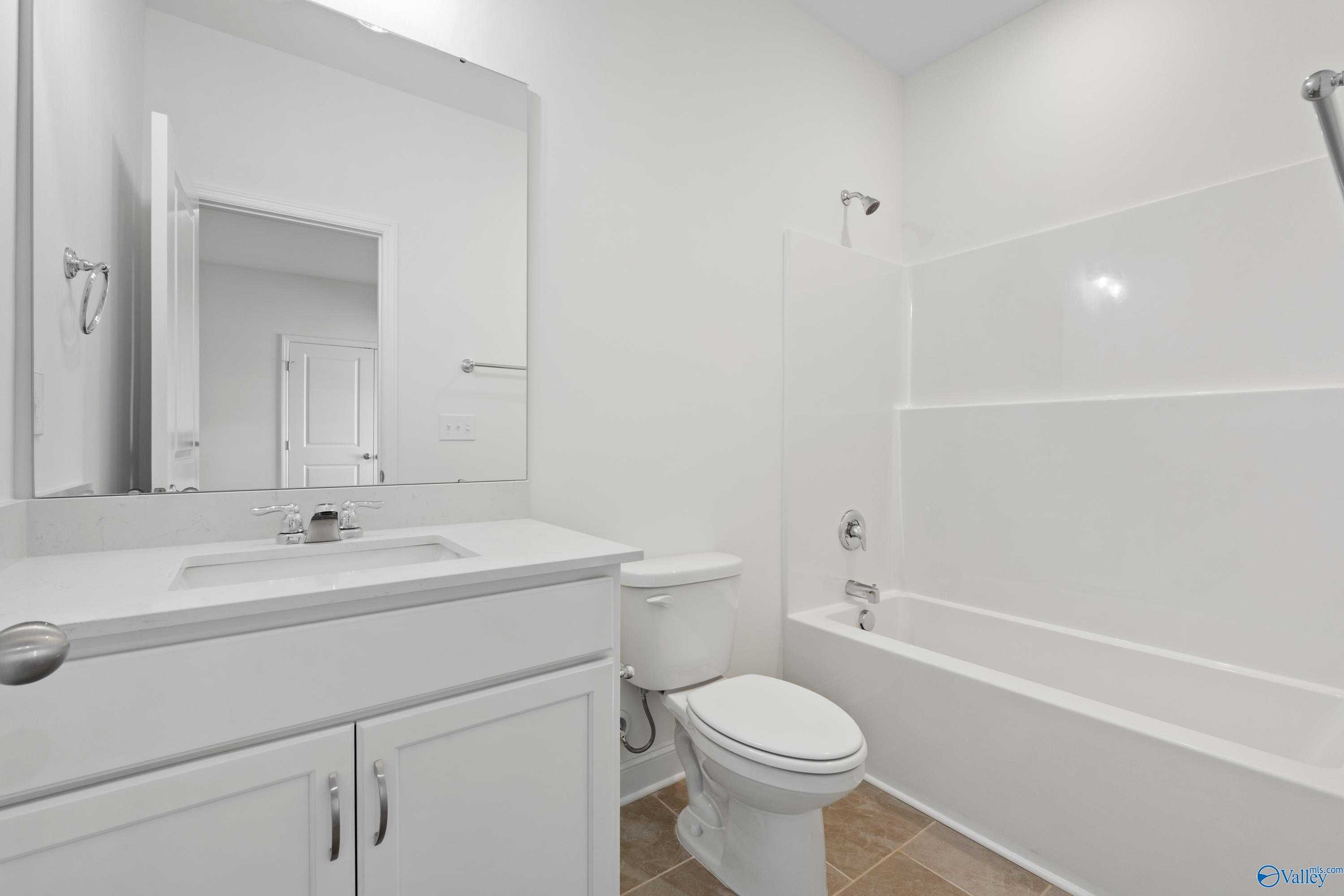 Bright white bathroom with bathtub, shower, vanity sink, mirror, and toilet in Davidson Homes The Oxford, Harvest, Alabama