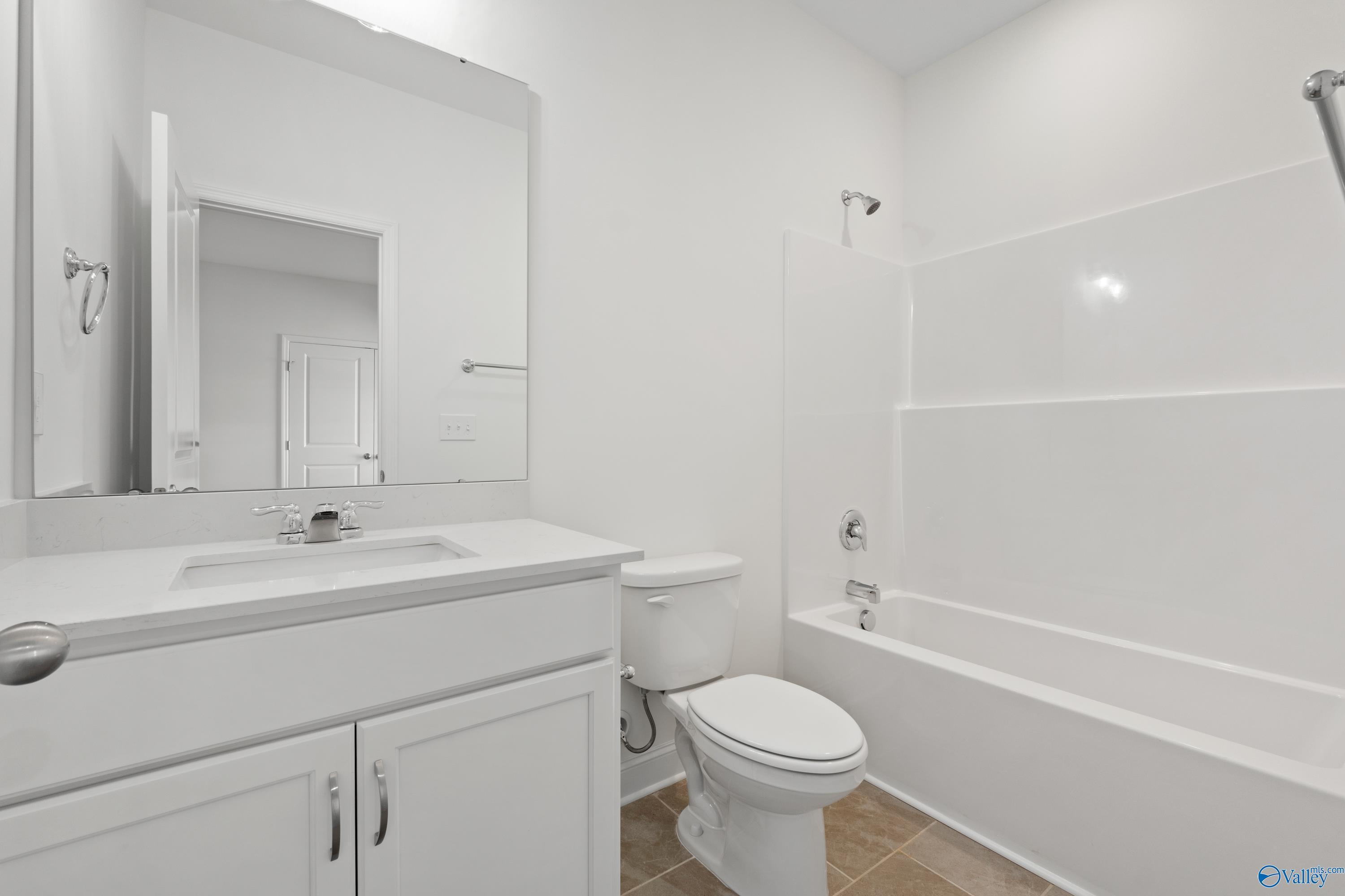 Bright white bathroom with bathtub, shower, vanity sink, mirror, and toilet in Davidson Homes The Oxford, Harvest, Alabama