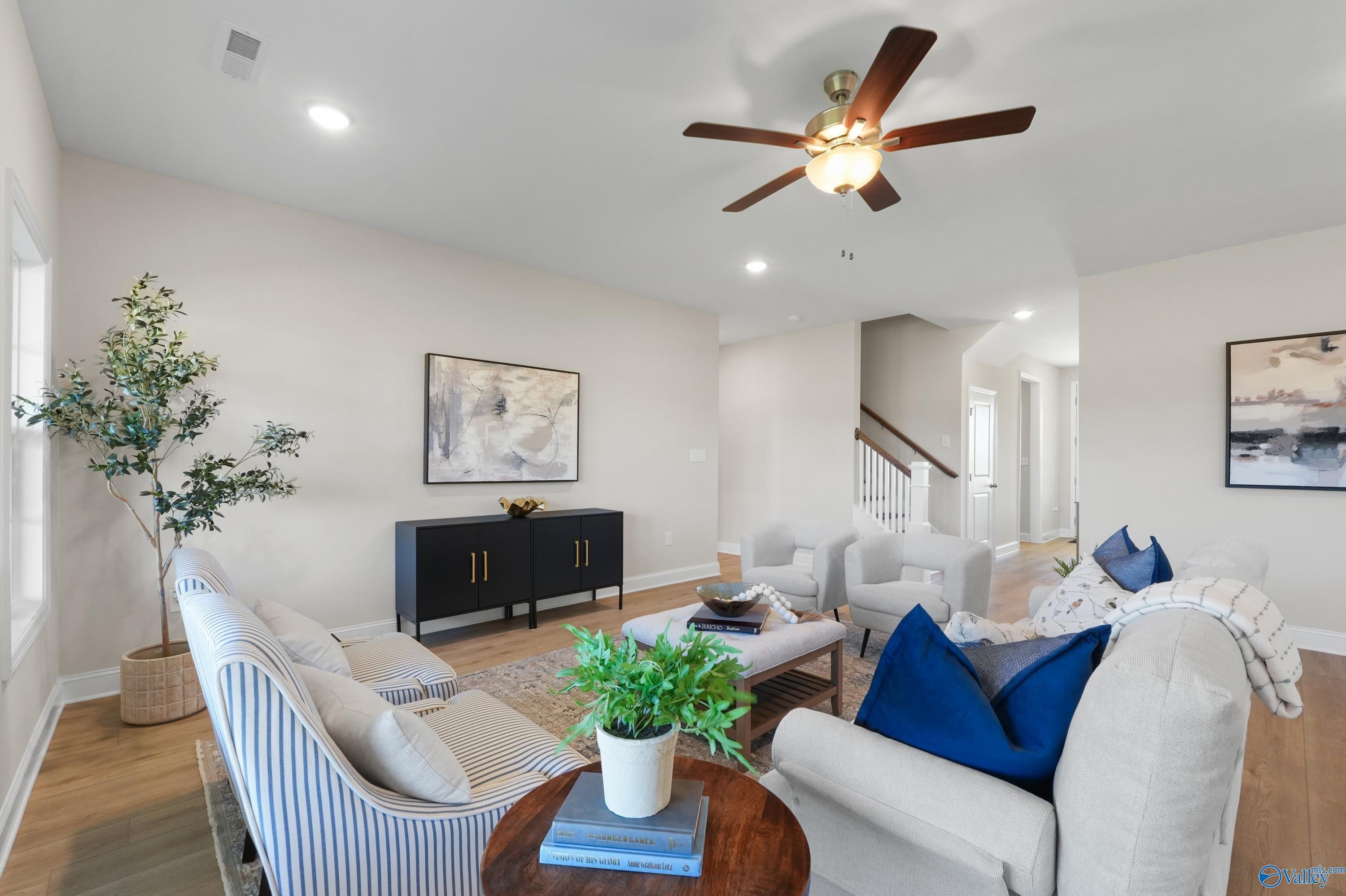 Cozy living room with beige sofa, blue pillows, striped armchair, potted plants, abstract art, and ceiling fan in Davidson Homes The Rockford B, Toney, Alabama