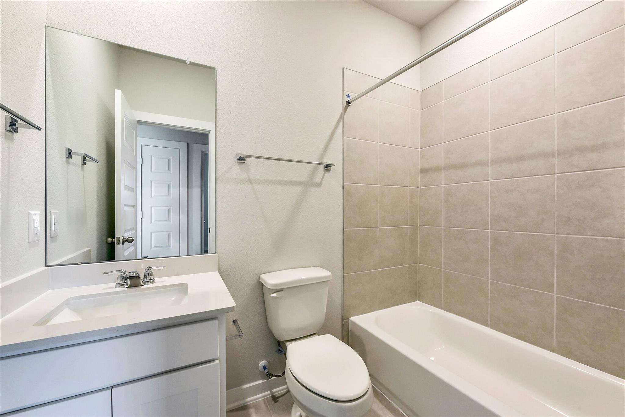 Modern secondary bathroom with white vanity, soaking tub, toilet, large mirror, and subway tile in Davidson Homes The Comal G, Dayton, Texas