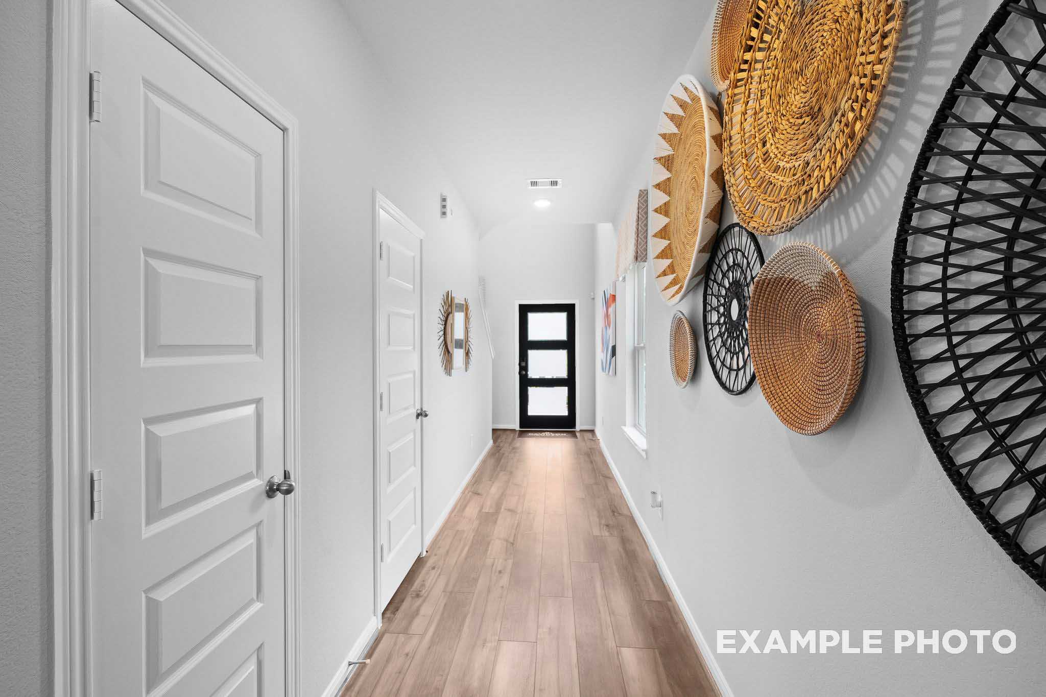 Spacious upper-floor hallway in The Trinity floor plan with hardwood floors, white doors, and woven wall art accents