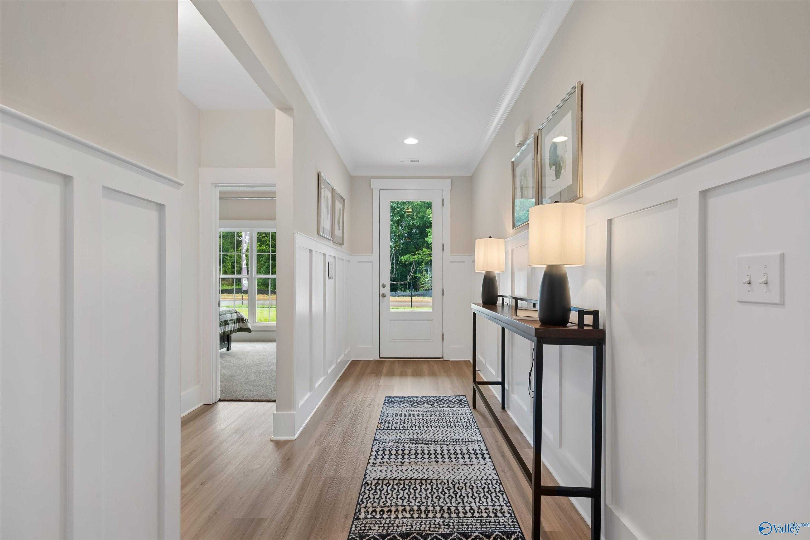 Elegant hallway with white wainscoting, hardwood floors, black console table, and lamps in Davidson Homes The Daphne, Durham Farms, Harvest, Alabama