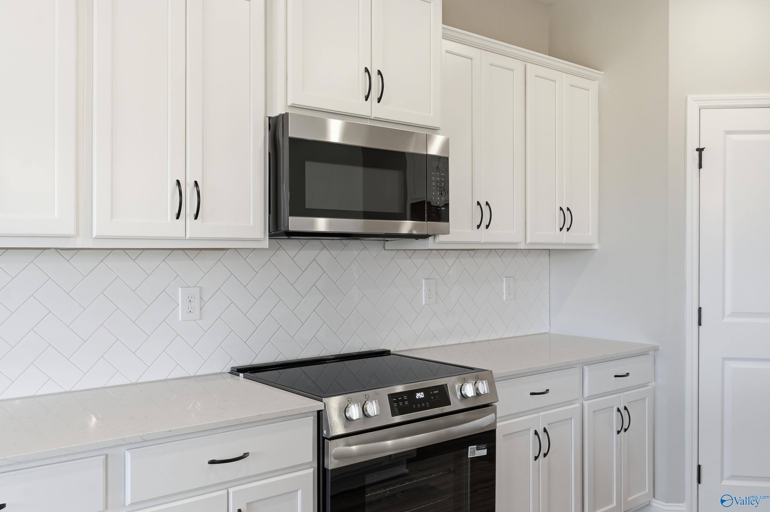Modern white kitchen with stainless steel oven, microwave, subway tile backsplash in Davidson Homes The Rockford, Harvest AL