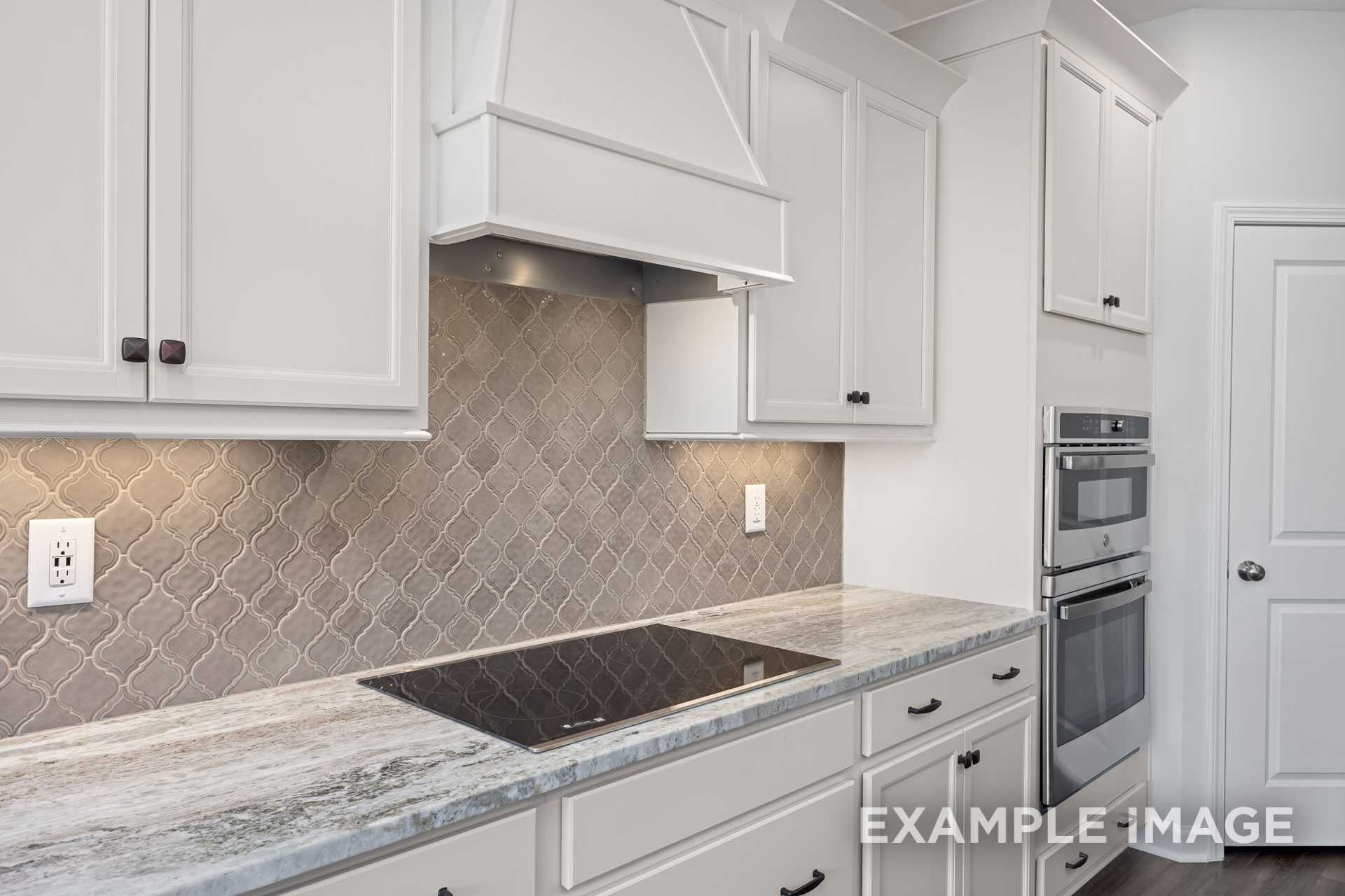 Modern kitchen in The Grace C with white shaker cabinets, gray mosaic tile backsplash, stainless steel double oven, and veined quartz counters