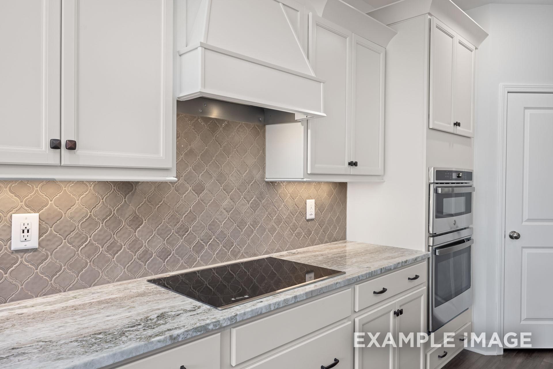 Modern kitchen in The Grace C with white shaker cabinets, gray mosaic tile backsplash, stainless steel double oven, and veined quartz counters