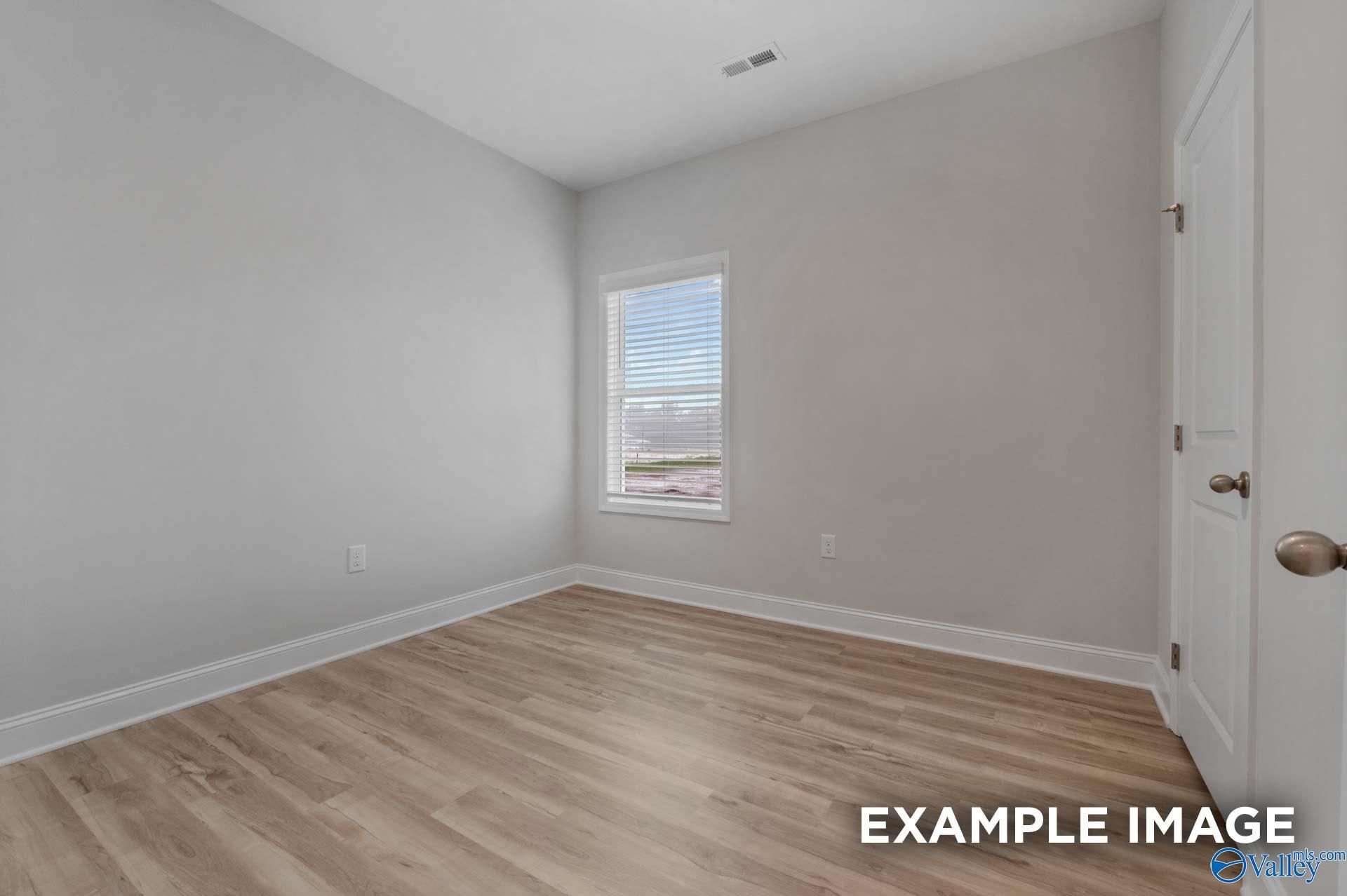 Bright secondary bedroom with gray walls, window blinds, white door, and laminate wood flooring in Davidson Homes The Cumberland B, Decatur AL