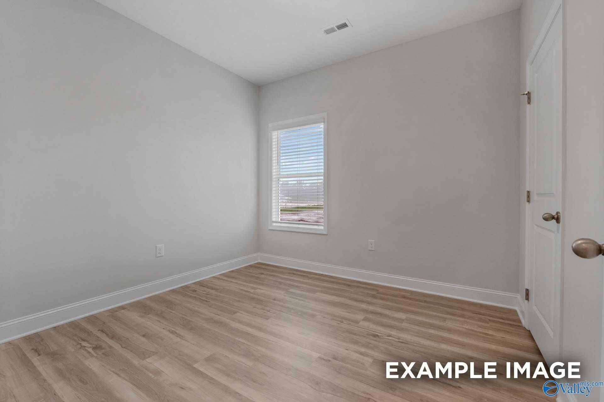 Bright secondary bedroom with gray walls, window blinds, white door, and laminate wood flooring in Davidson Homes The Cumberland B, Decatur AL