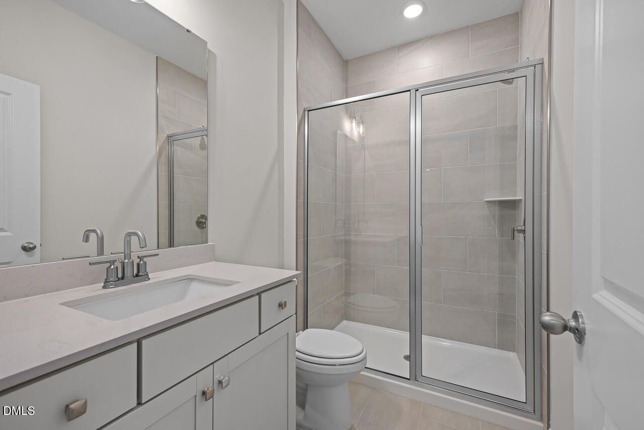 Modern bathroom with glass-enclosed shower, stone vanity, and neutral tile in The Ashport G by Davidson Homes, Wake Forest.