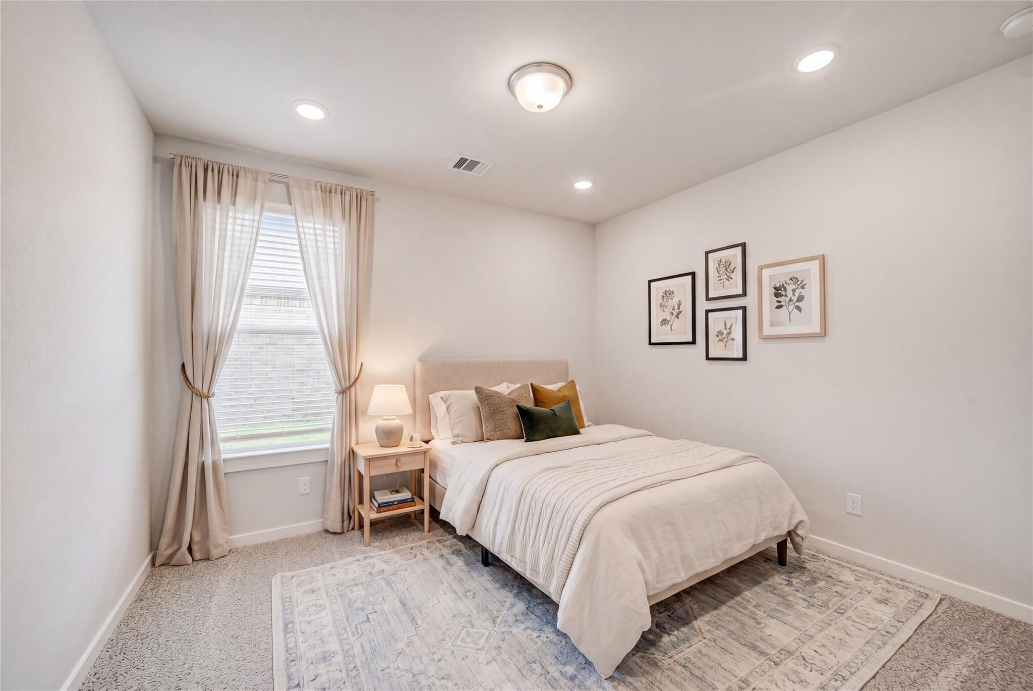 Cozy bedroom with plush white bed, green pillows, botanical wall art, sheer curtains, and recessed lighting in Davidson Homes The Acadia C, Magnolia Texas