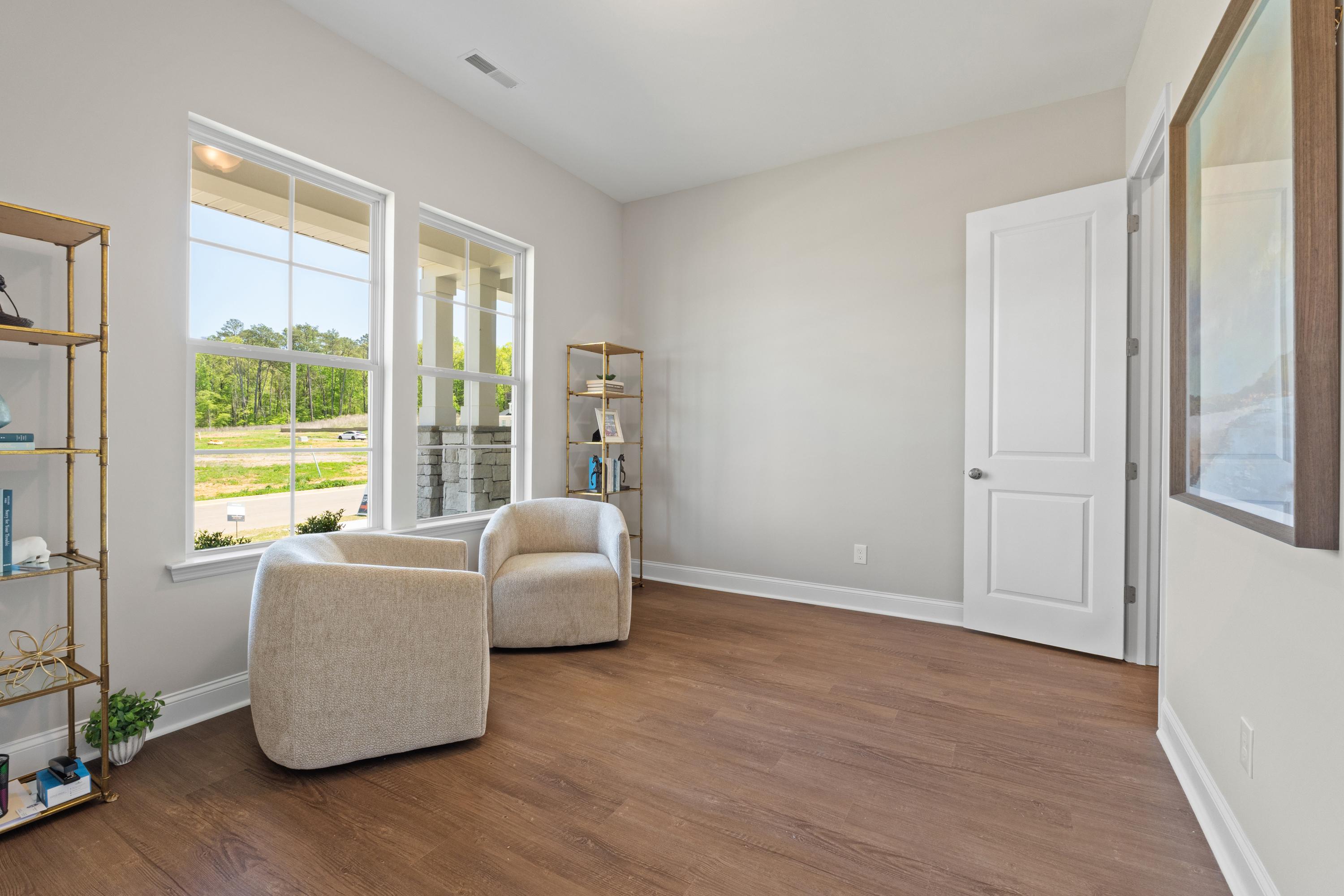 Cozy study in The Haven D home design with beige armchairs, bookshelves, and large windows overlooking trees