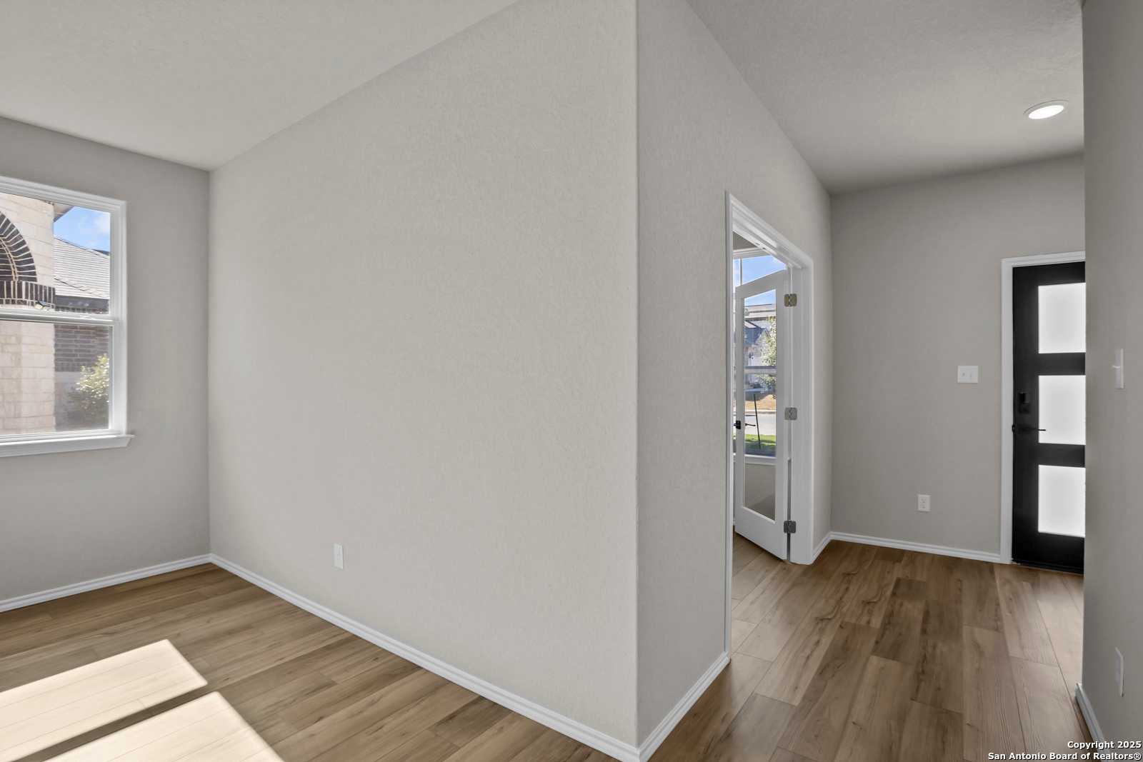 Bright bedroom with light gray walls, hardwood floors, large window, and glass-paneled doors in Davidson Homes The Murray F, Converse TX