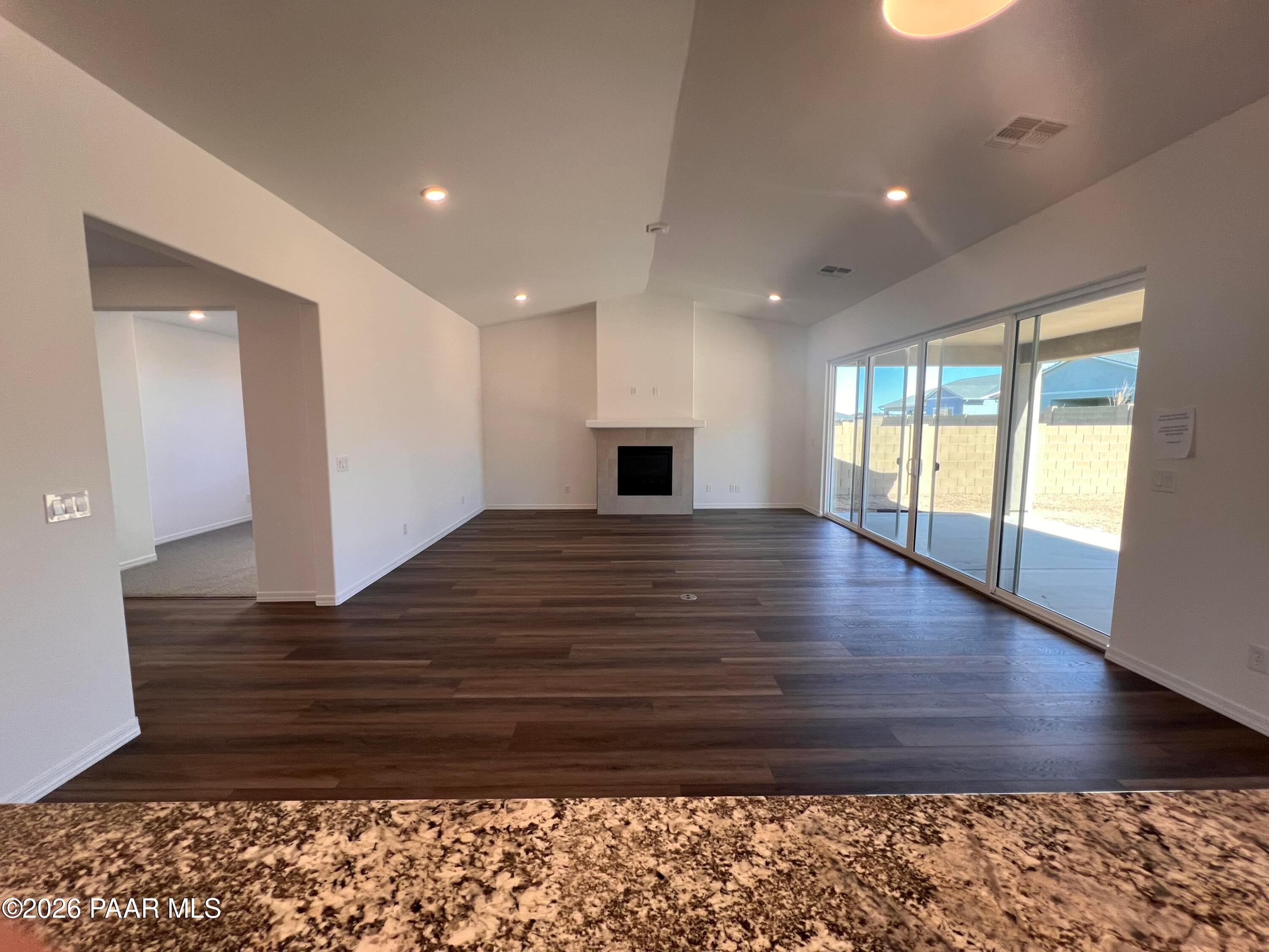 Open-concept living room with stone fireplace, hardwood floors, and sliding glass doors to patio in Davidson Homes The Sunrise II A, Prescott, AZ