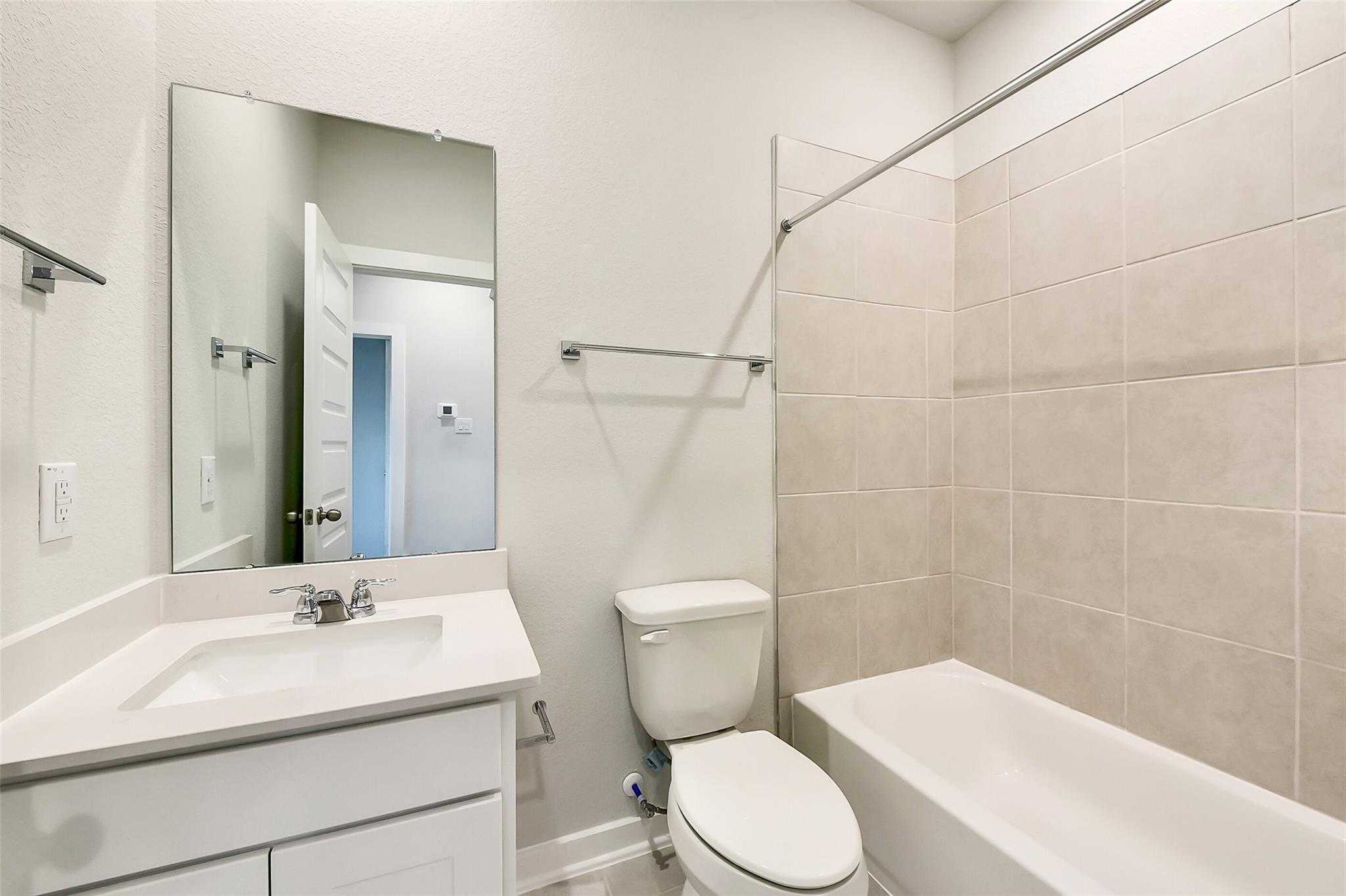 Modern bathroom with white vanity, soaking tub, tiled shower, and toilet in Davidson Homes The Frio G, Dayton, Texas