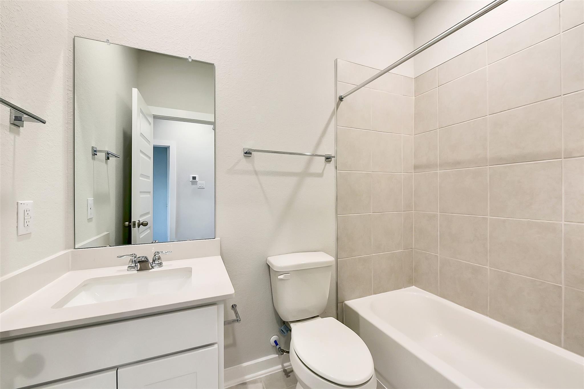 Modern bathroom with white vanity, bathtub shower combo, and neutral tiles in Davidson Homes The Frio G, Dayton, Texas