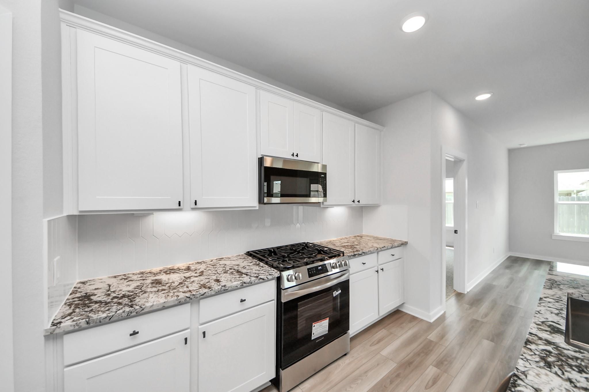 Modern white kitchen with granite countertops and stainless appliances in The Everett C floor plan, River Ranch Meadows.