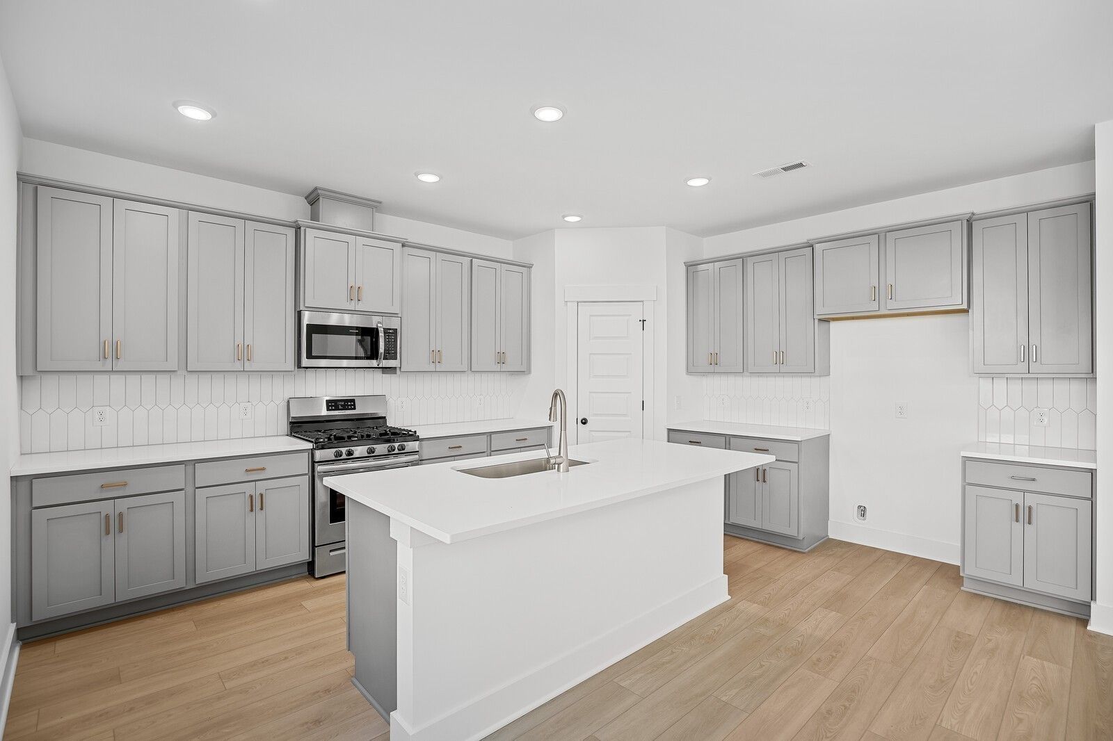 Modern kitchen featuring gray shaker cabinets, white quartz island with sink, stainless appliances in Davidson Homes The Logan C, Gallatin, TN