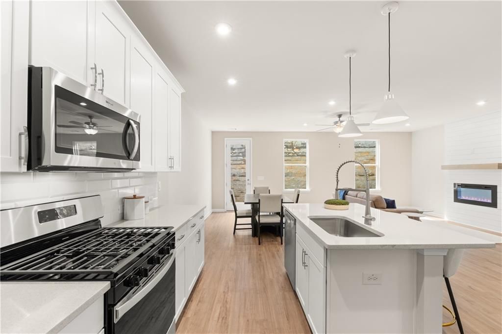 Modern open-concept kitchen with white cabinets, stainless appliances, quartz island, and adjacent dining area in Davidson Homes The Marion B, Kennesaw, GA