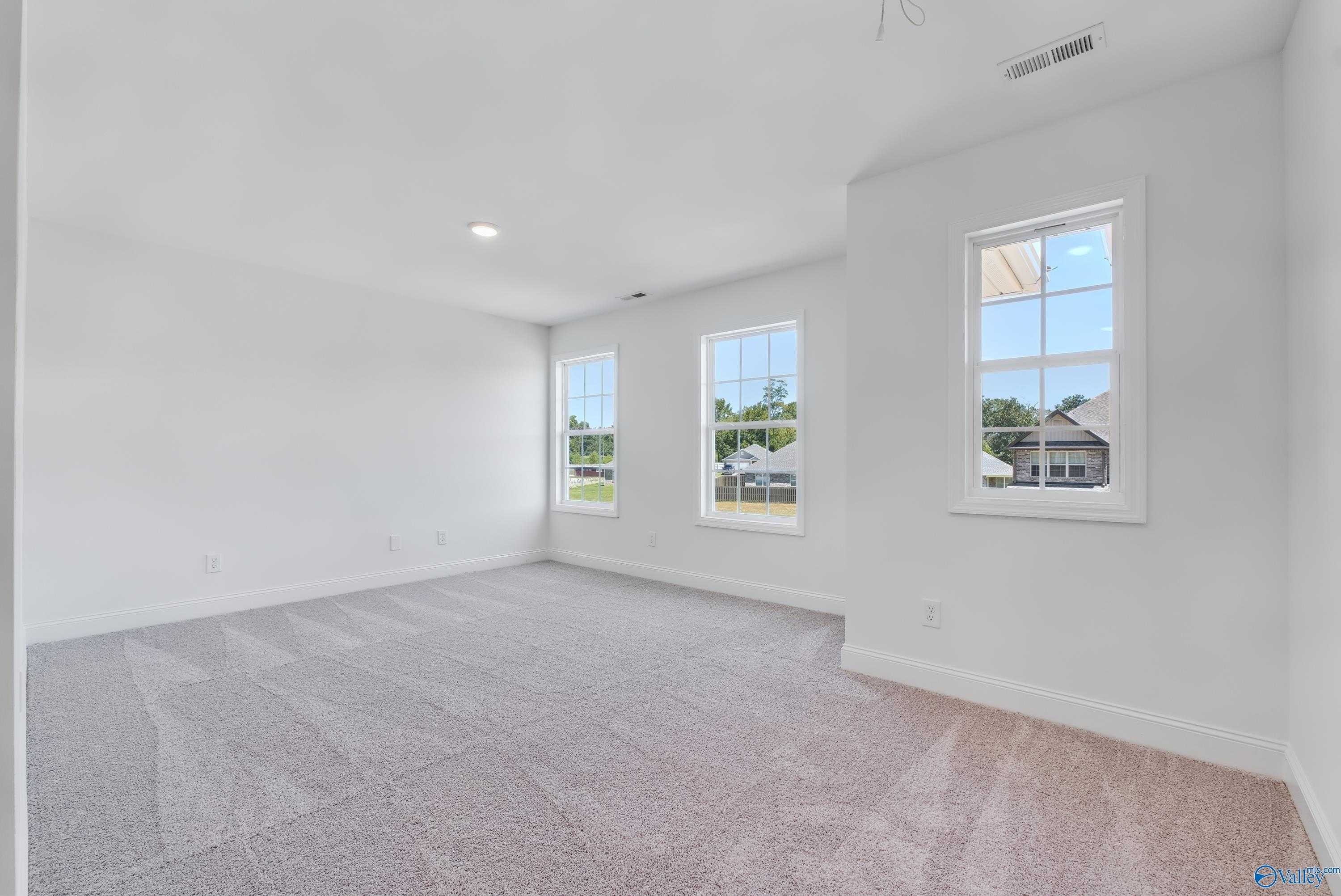 Spacious empty bedroom with large windows, white walls, beige carpet in Davidson Homes The Shelby A, Arab, Alabama