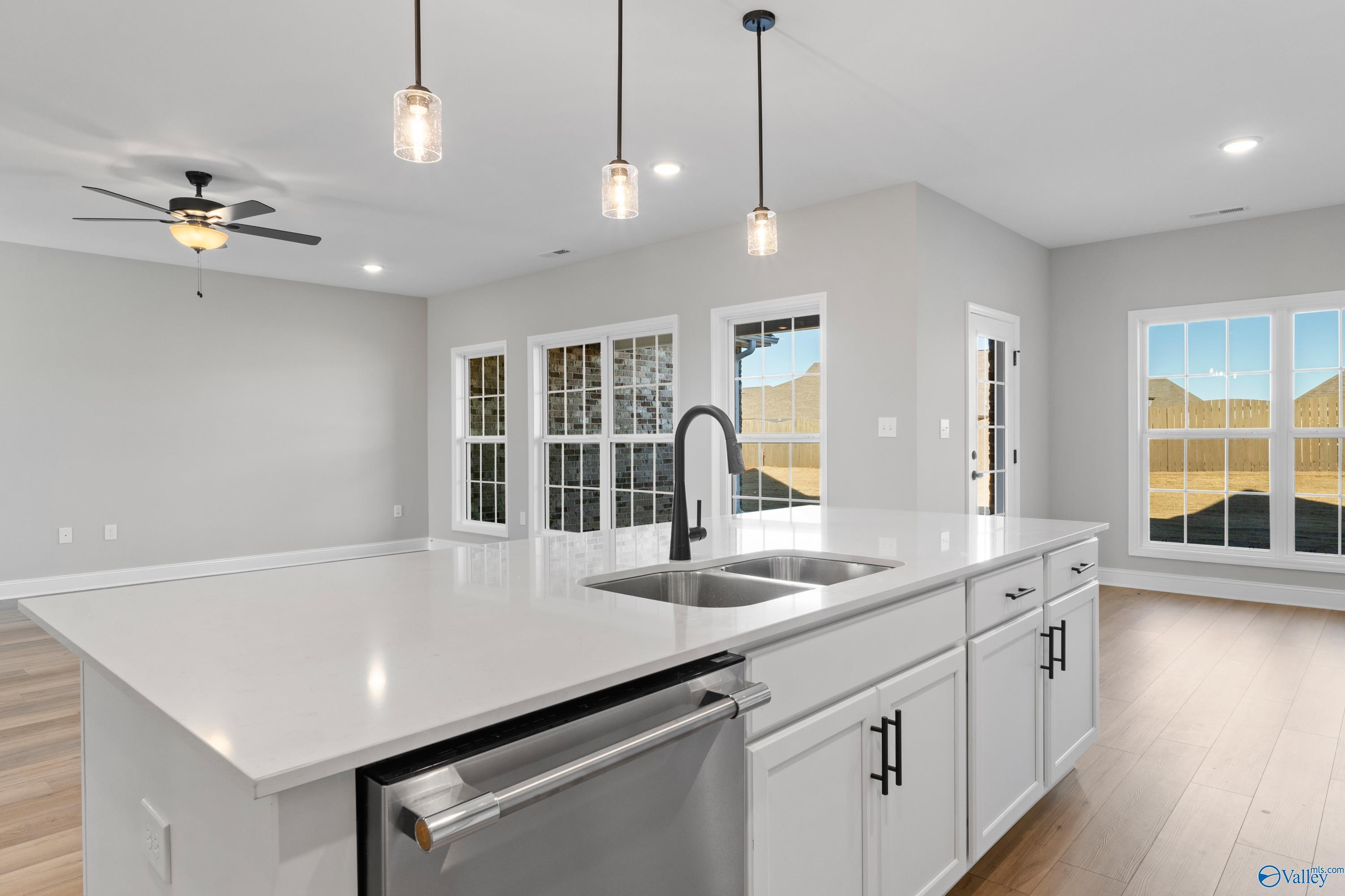 Modern white kitchen island with double sink, stainless dishwasher, pendant lights, and large windows in The Valencia by Davidson Homes, Meridianville