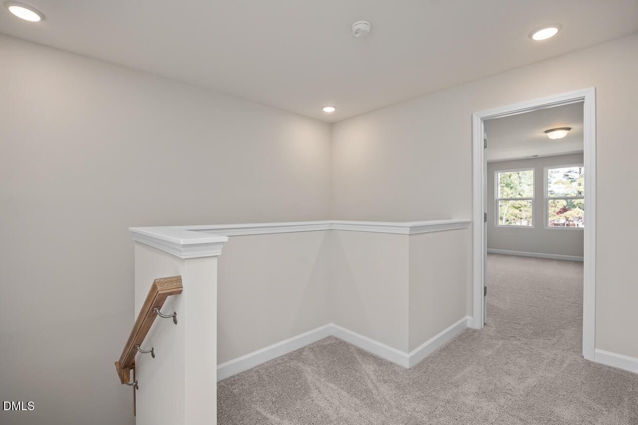 Spacious upstairs hallway with beige walls, white railing overlook, and recessed lights in Davidson Homes The Graham, Fuquay-Varina, NC