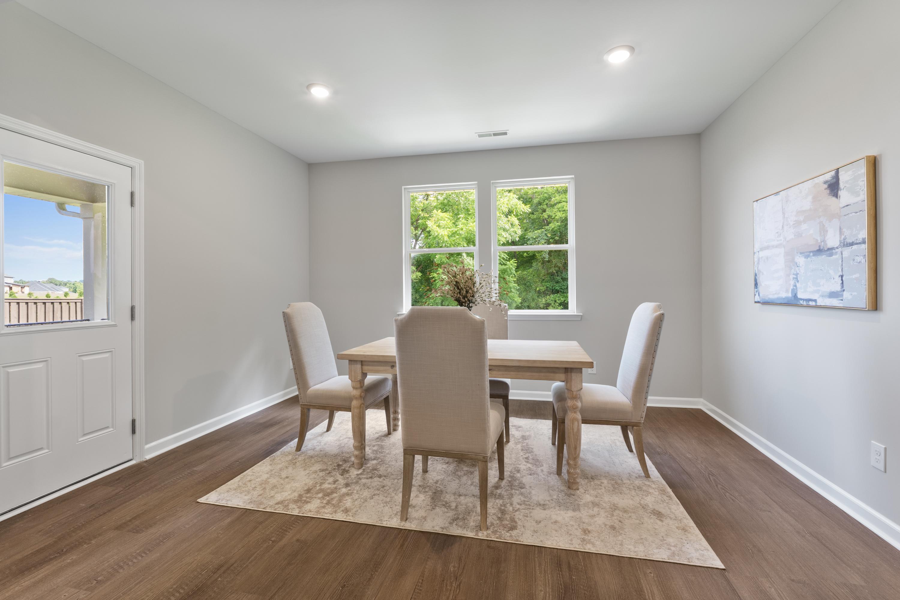 Spacious dining room in The Avalon D featuring wooden table, upholstered chairs, area rug, and large windows with green views