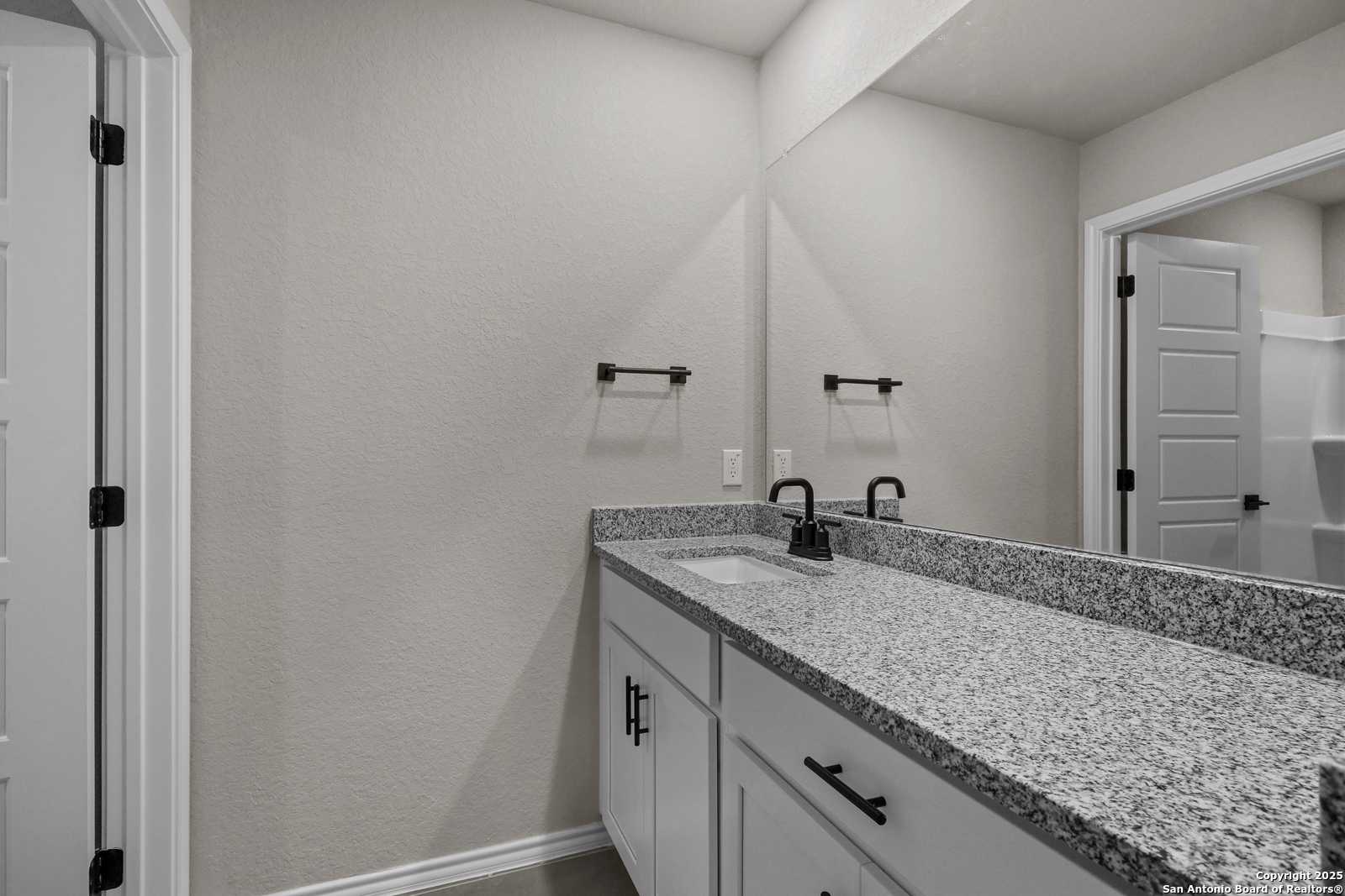 Modern master bathroom featuring double granite vanity, black faucets, and frameless mirror in Davidson Homes Charlotte B, San Antonio