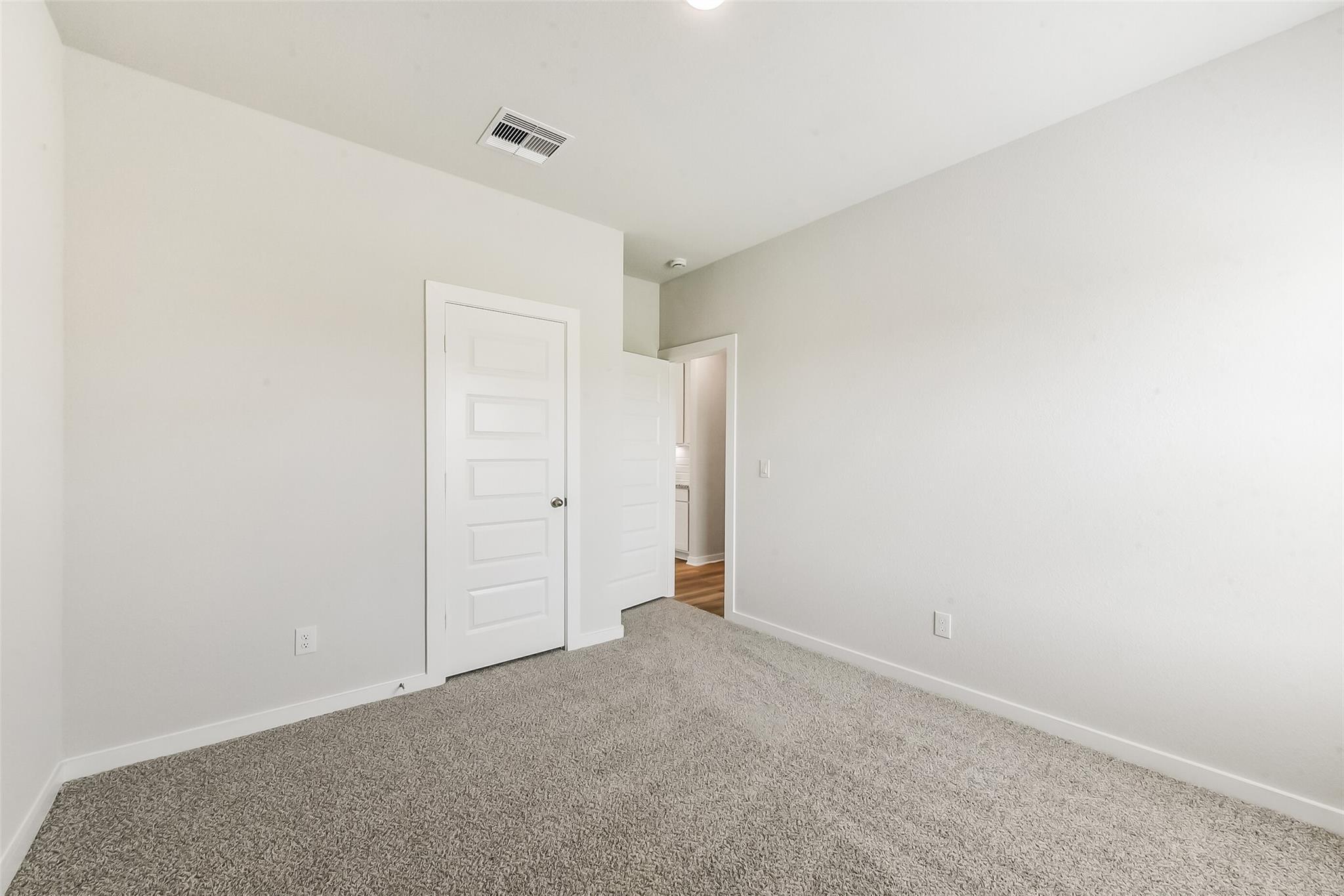Spacious secondary bedroom with beige carpet, light gray walls, and attached bathroom in Davidson Homes The Frio G, Magnolia, Texas