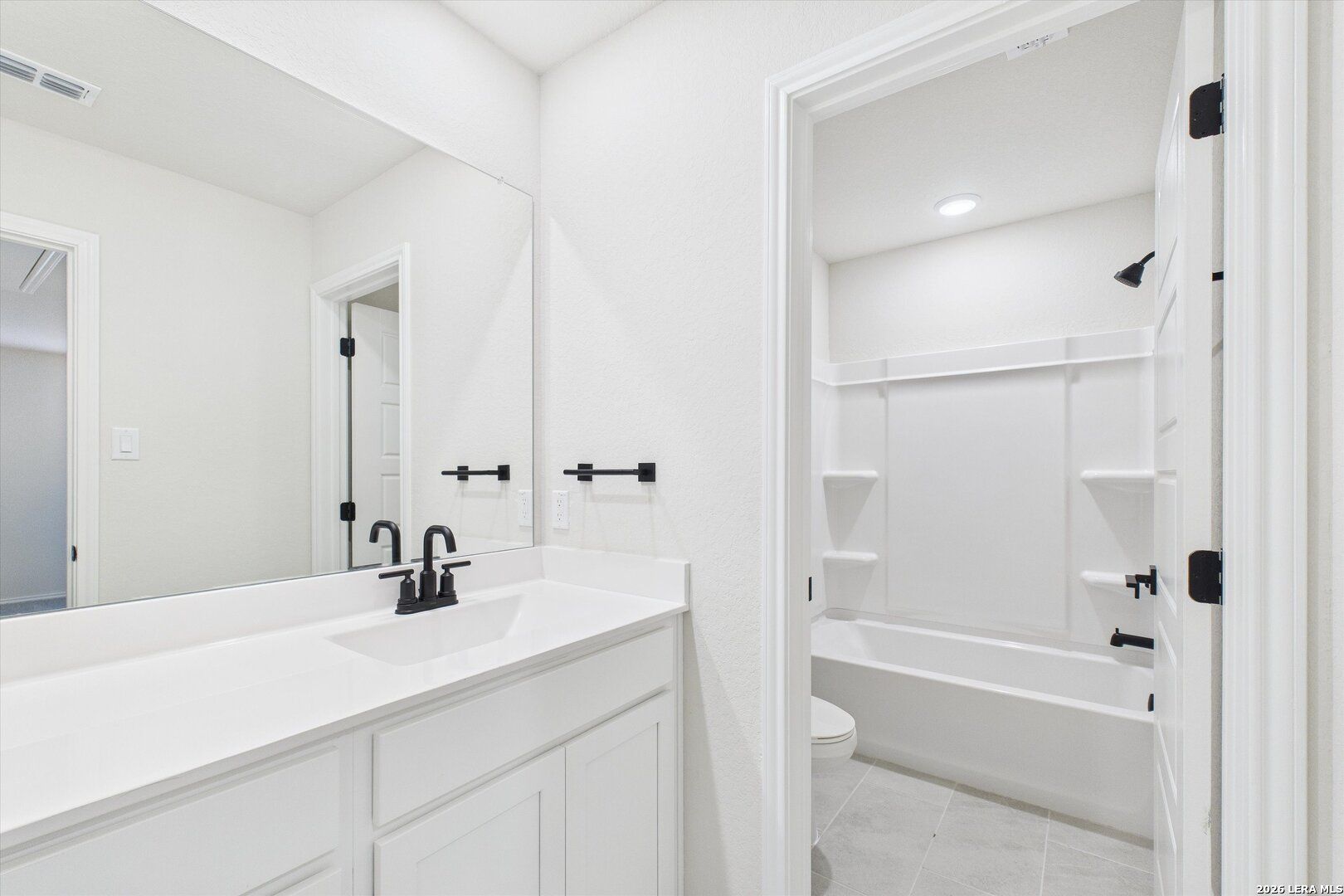 Bright white bathroom with single vanity, large mirror, and tub-shower combo in The Gillian B by Davidson Homes, San Antonio