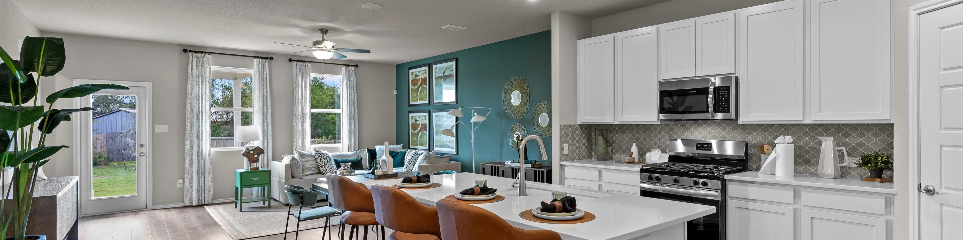 Open-concept kitchen and living area in Comanche Ridge San Antonio home by Davidson Homes with white cabinets, island bar, hardwood floors